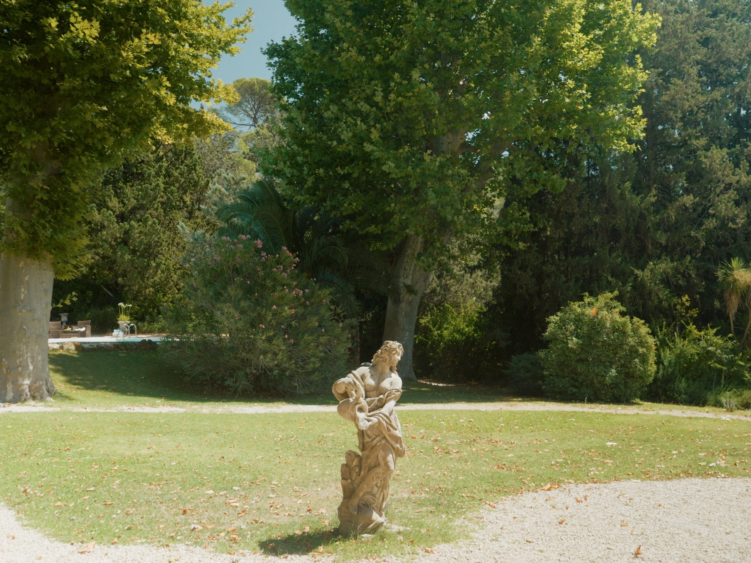 A garden scene at Chateau Robernier with a marble sculpture of a woman and a child, surrounded by trees and lush greenery.