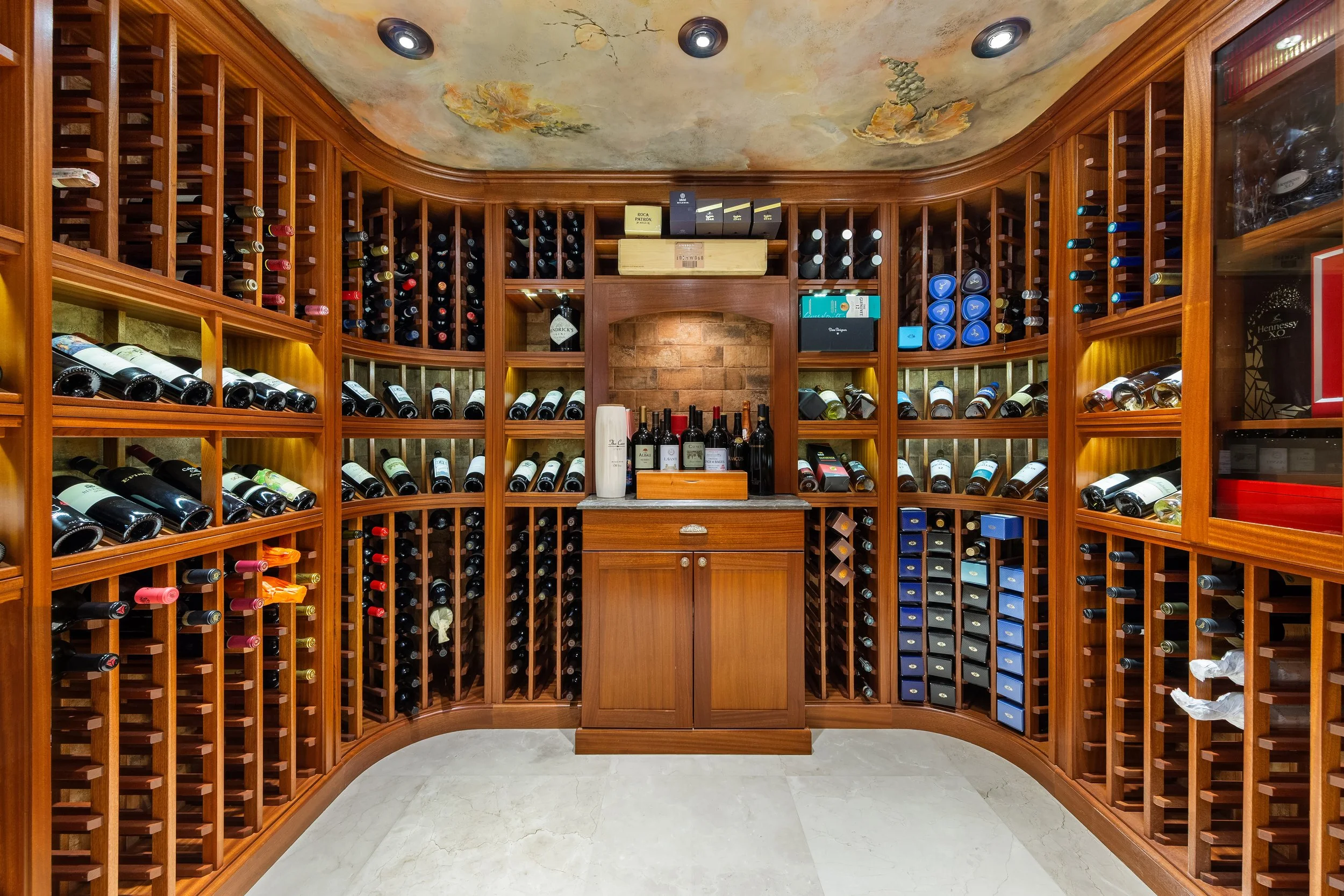 A luxurious wine cellar with wooden wine racks filled with bottles, a wooden countertop, and a ceiling with ornate painted decoration.