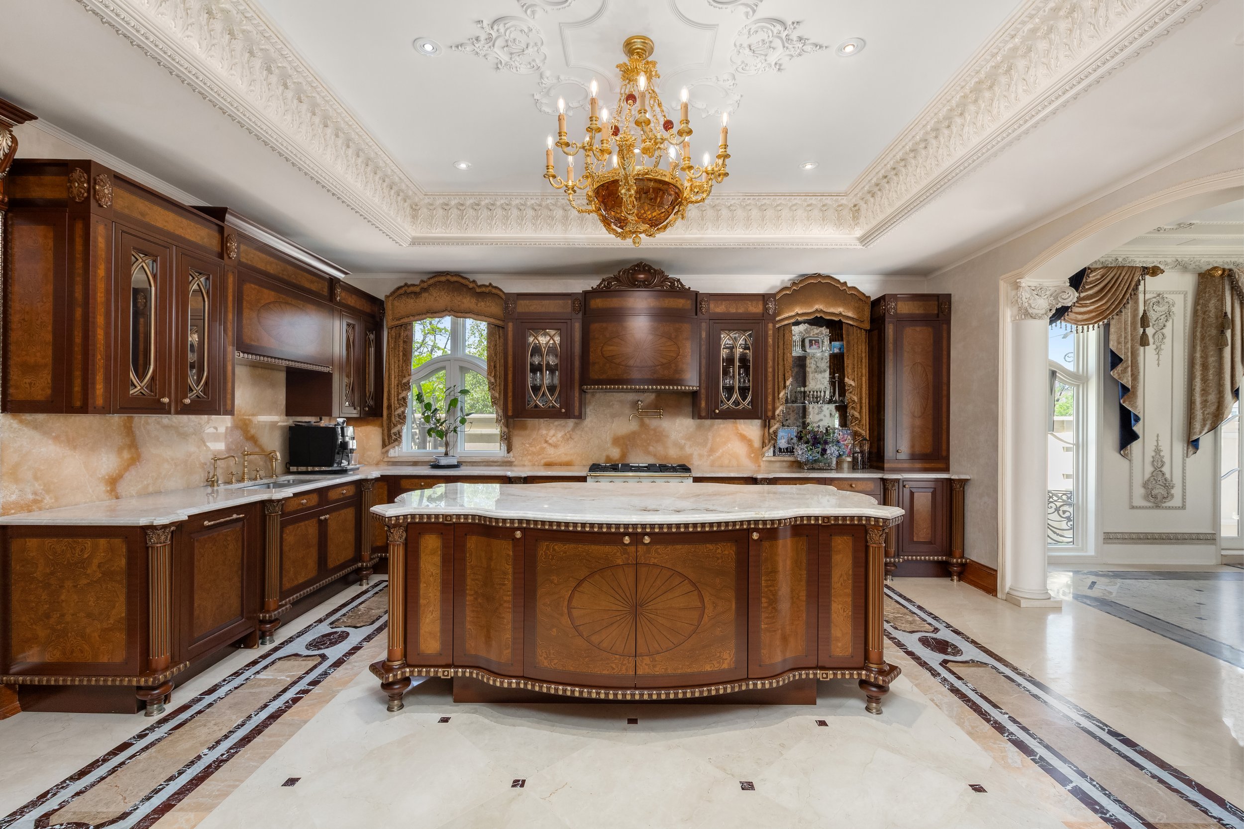 Elegant kitchen with dark wood cabinetry, marble countertops, a central island, a chandelier, and large windows with draped curtains.