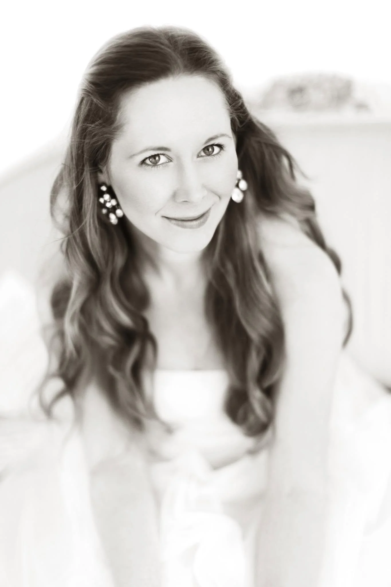 Black and white portrait of a woman with long, wavy hair, wearing earrings, smiling slightly, and looking at the camera.