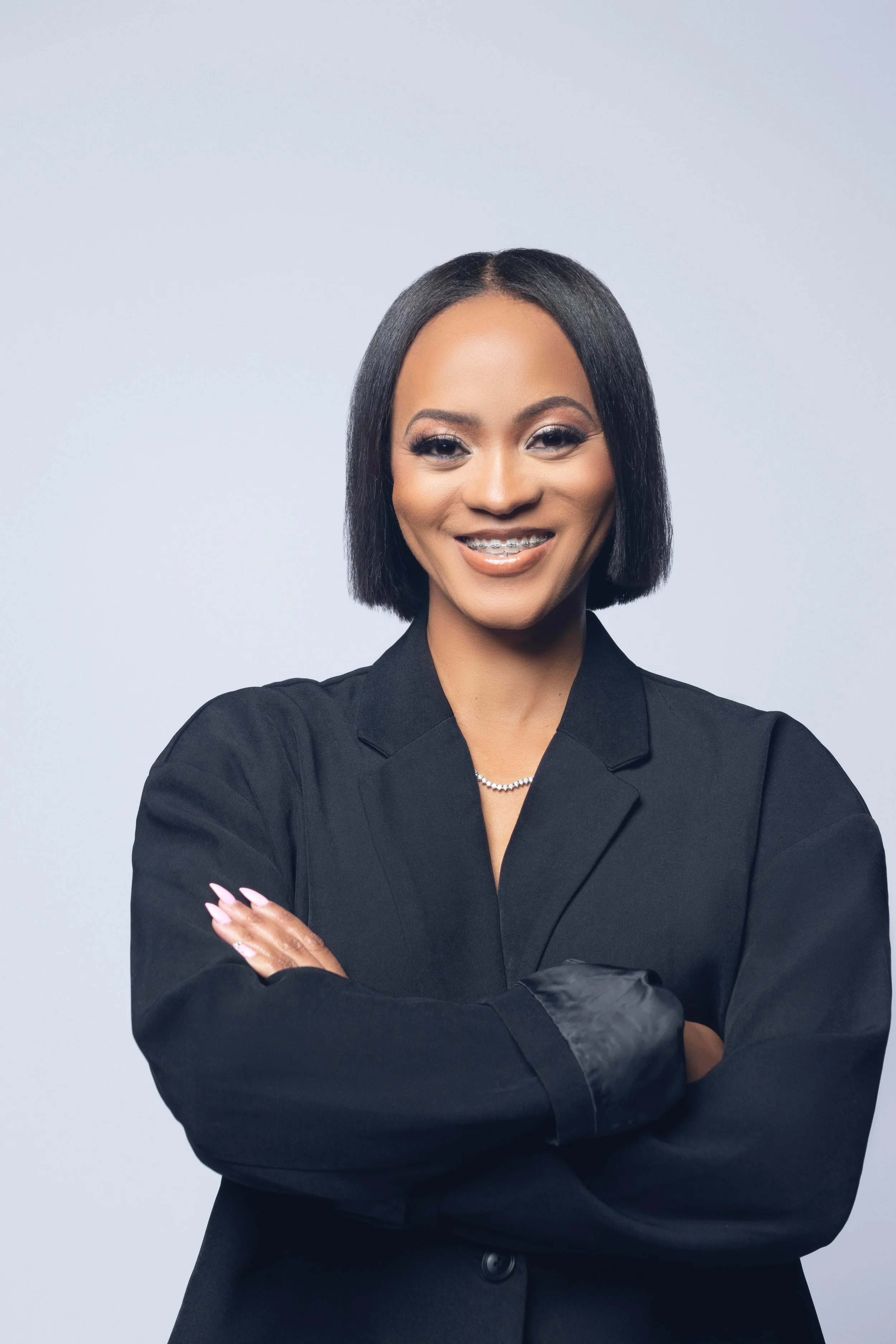 A woman in a black suit with crossed arms, smiling, against a light gray background.