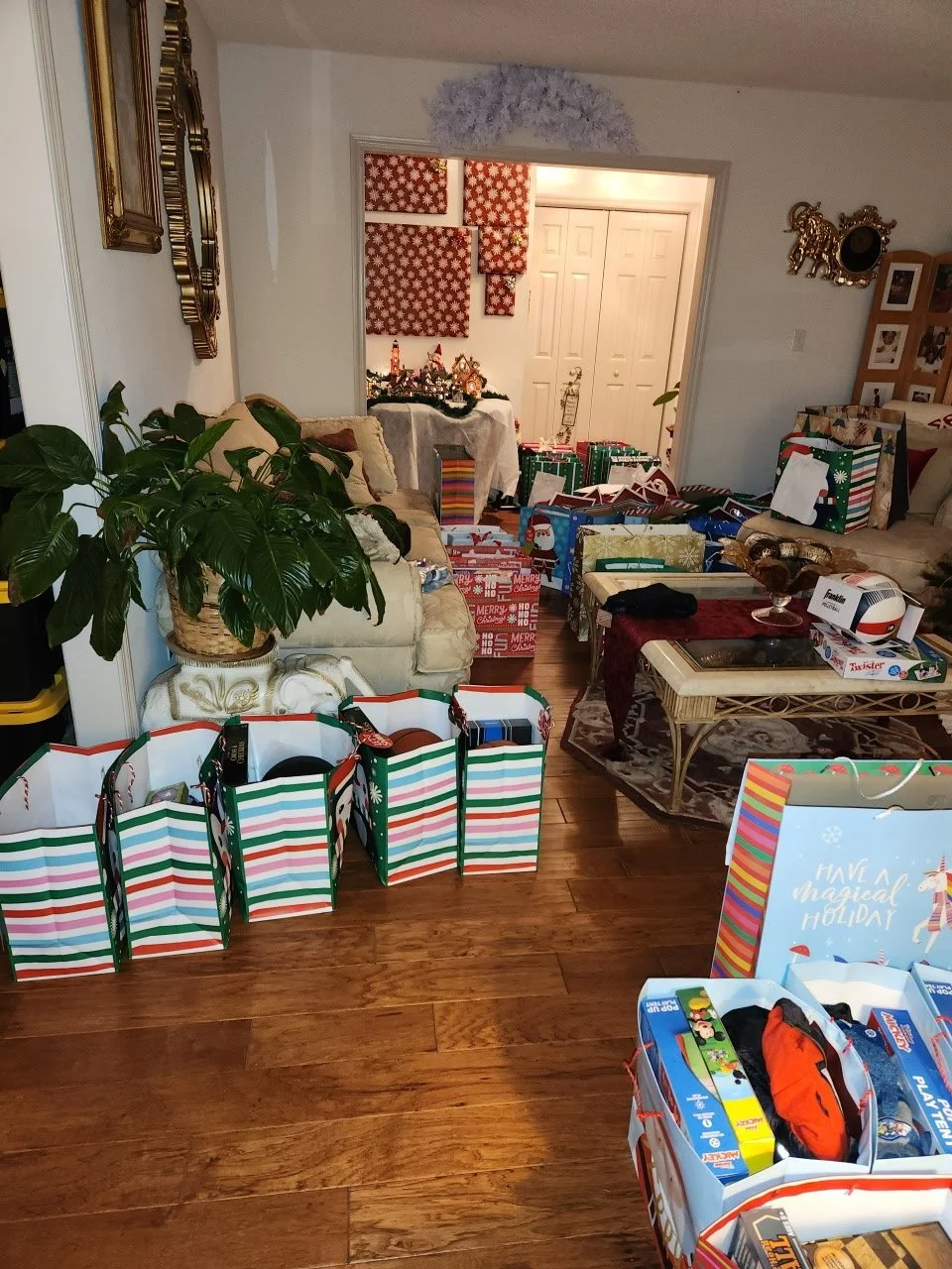 Living room filled with Christmas presents and decorations, including gift bags, boxes, and holiday-themed wall art.