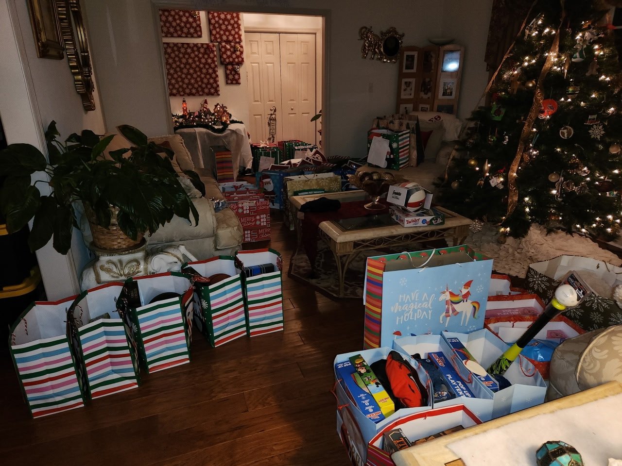 Living room decorated for Christmas with a lit Christmas tree, wrapped gifts, and holiday decorations on furniture and tables.