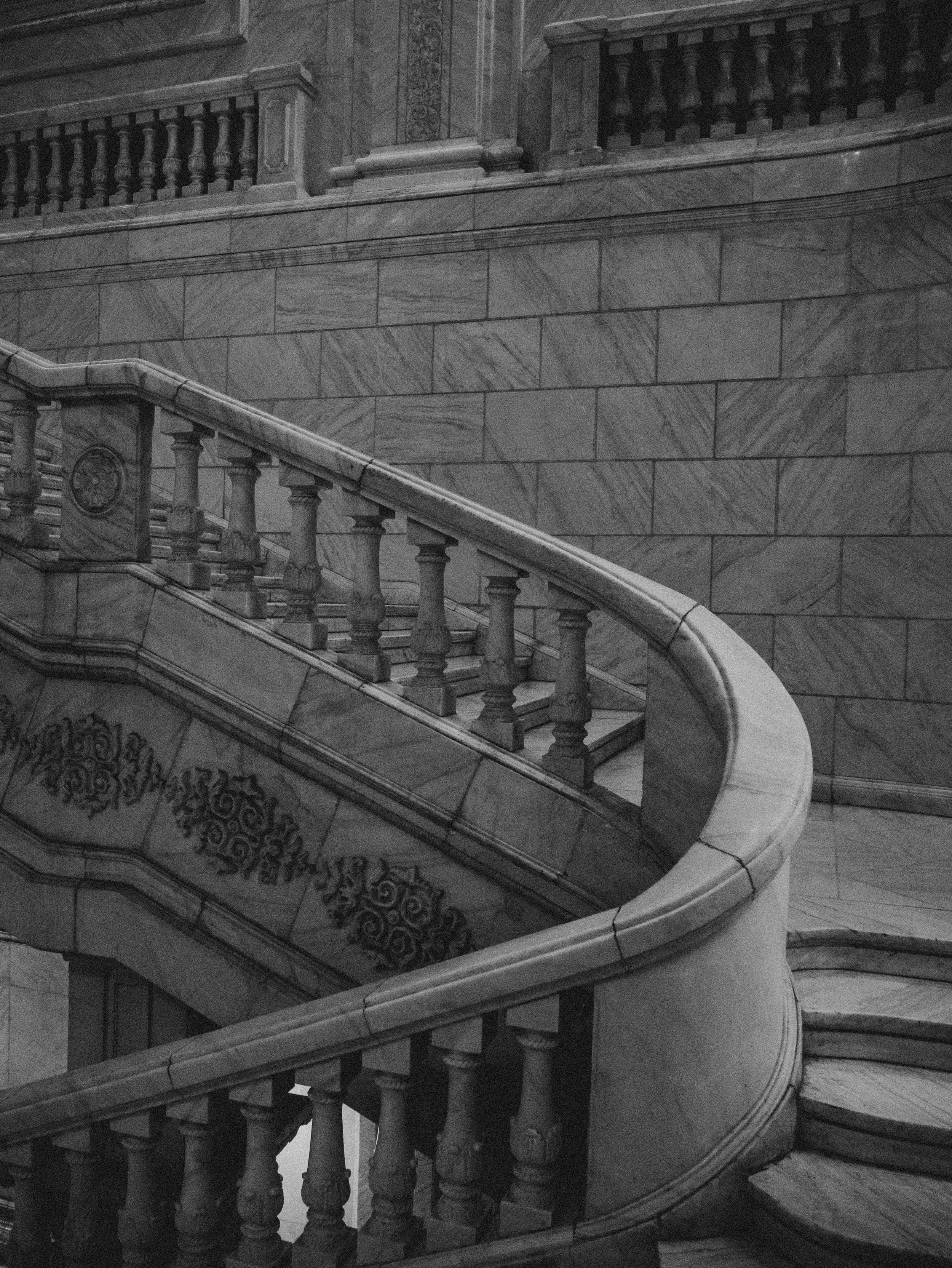 Black and white photo of a grand marble staircase with intricate railings and ornate decoration on the wall.
