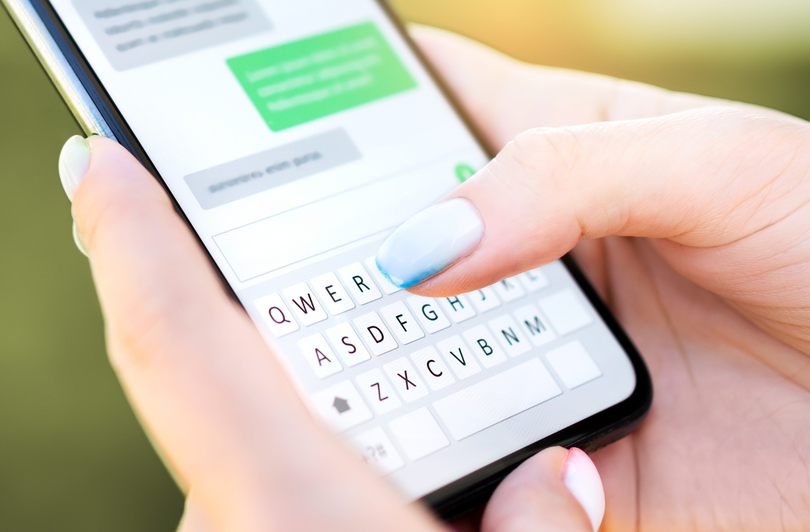 Close-up of a person's hand with painted nails using a smartphone touchscreen, typing a message with a white keyboard overlay on the screen.