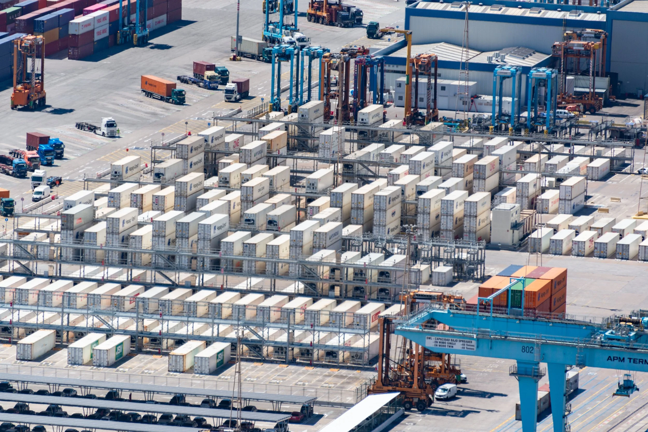 An aerial view of a port cargo terminal with numerous shipping containers, cranes, trucks, and equipment for loading and unloading ships.