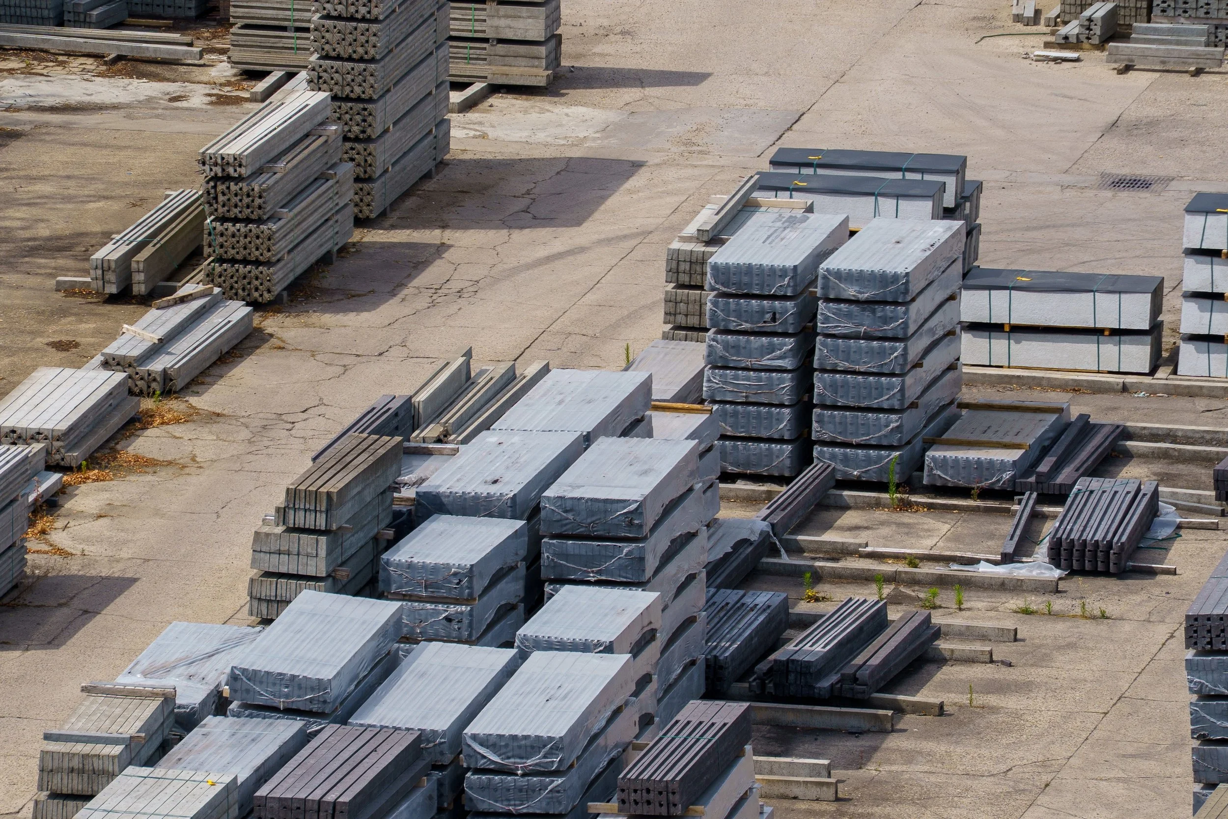 Stacks of gray concrete and metal construction materials stored on a paved lot.