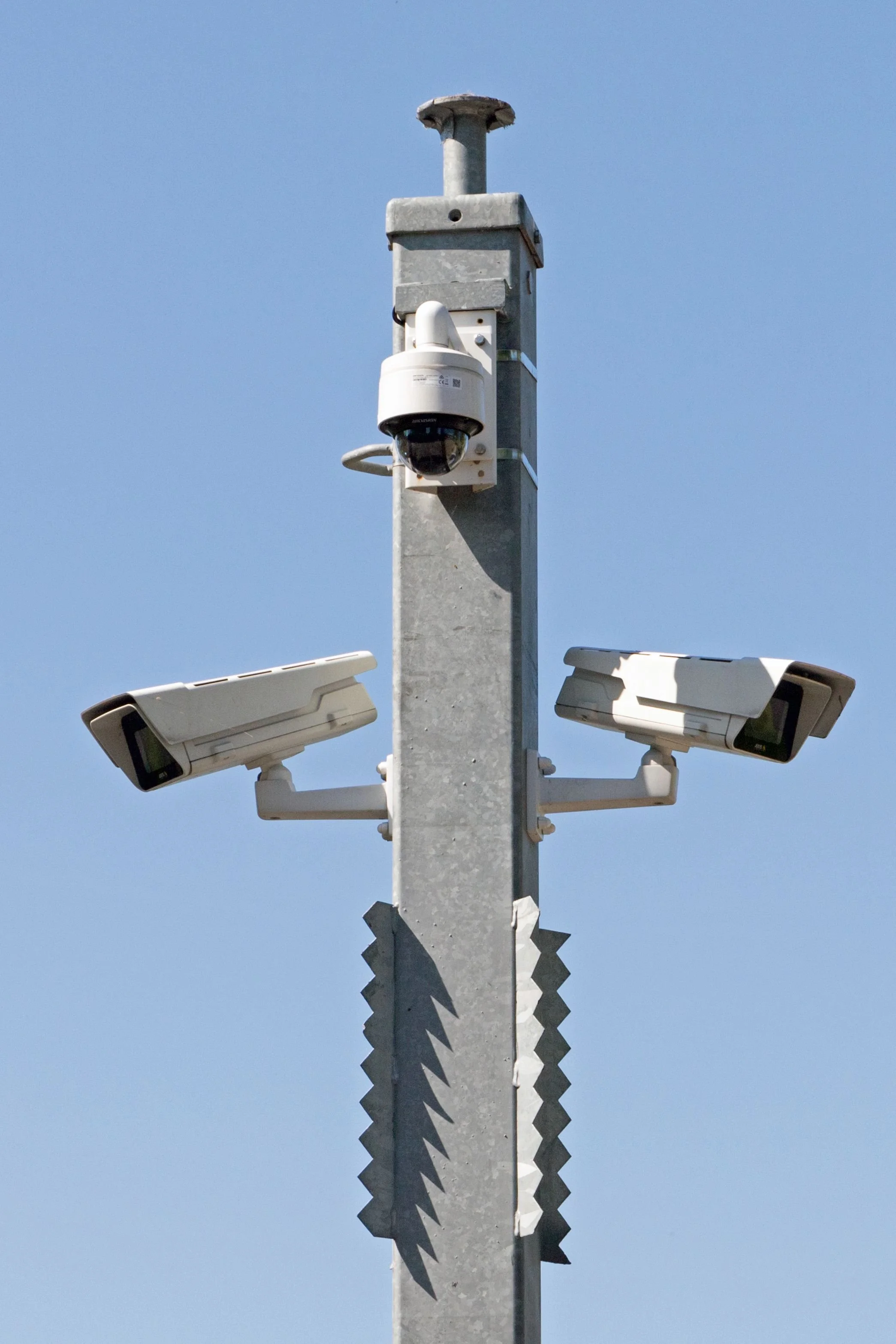 Security cameras mounted on a metal pole against a clear blue sky.