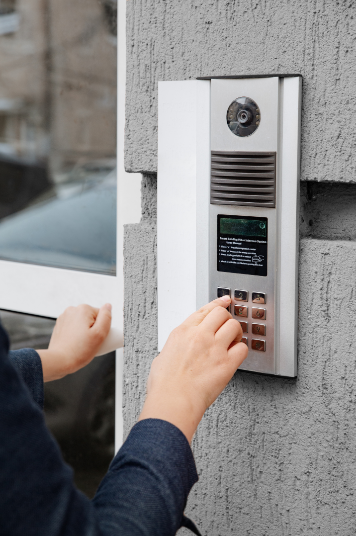 Person entering a code on an intercom system mounted on a gray brick wall.