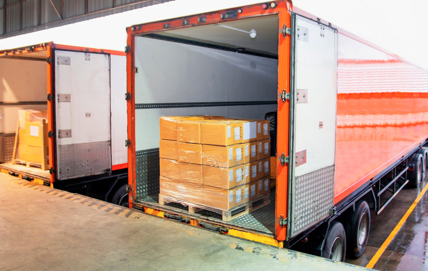 Open orange delivery truck with boxes on pallets inside and on the ramp outside.