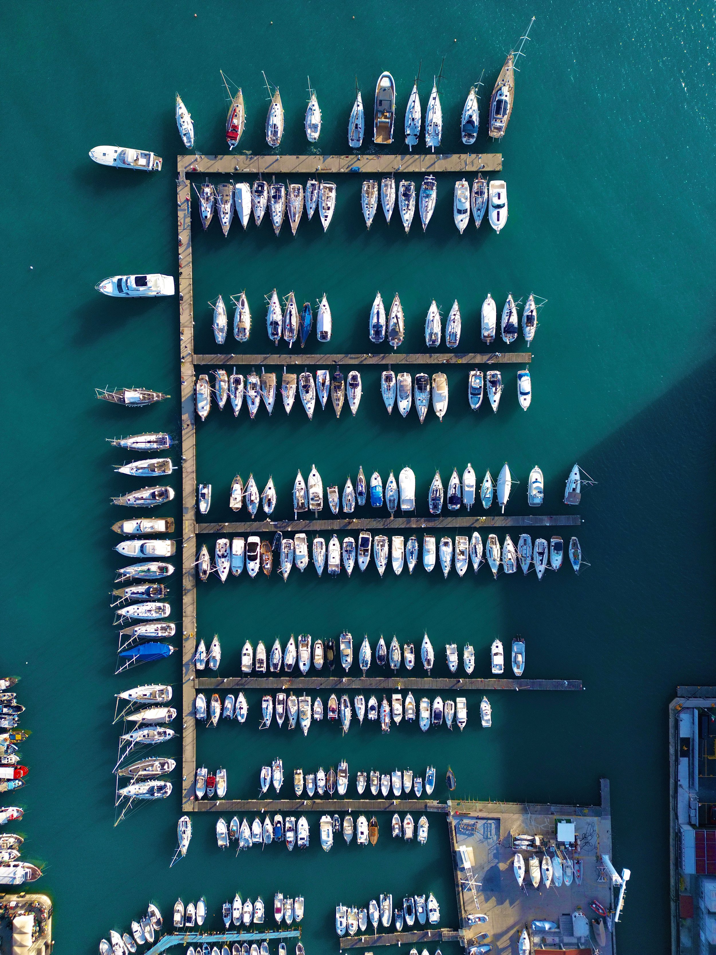 Aerial view of a marina with multiple boats docked, arranged in rows on water surrounded by piers and structures.
