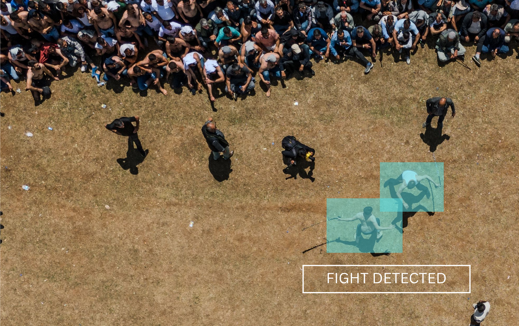 An aerial view of a large crowd of people standing in line, with three individuals identified as involved in a fight on the grass field near the bottom right, highlighted with blue boxes and labeled 'FIGHT DETECTED'.