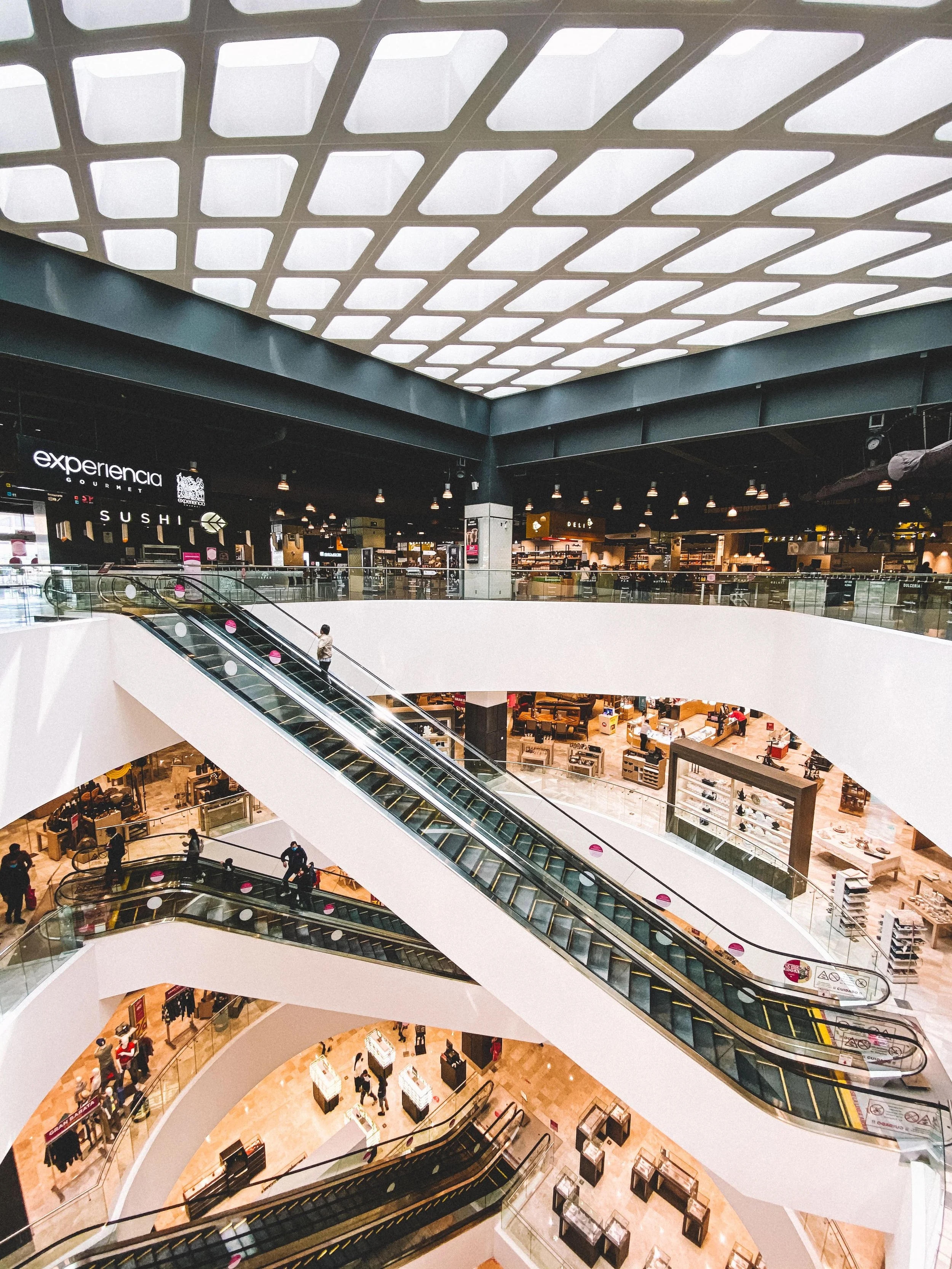 Interior of a multi-level shopping mall with escalators, storefronts, and shoppers.