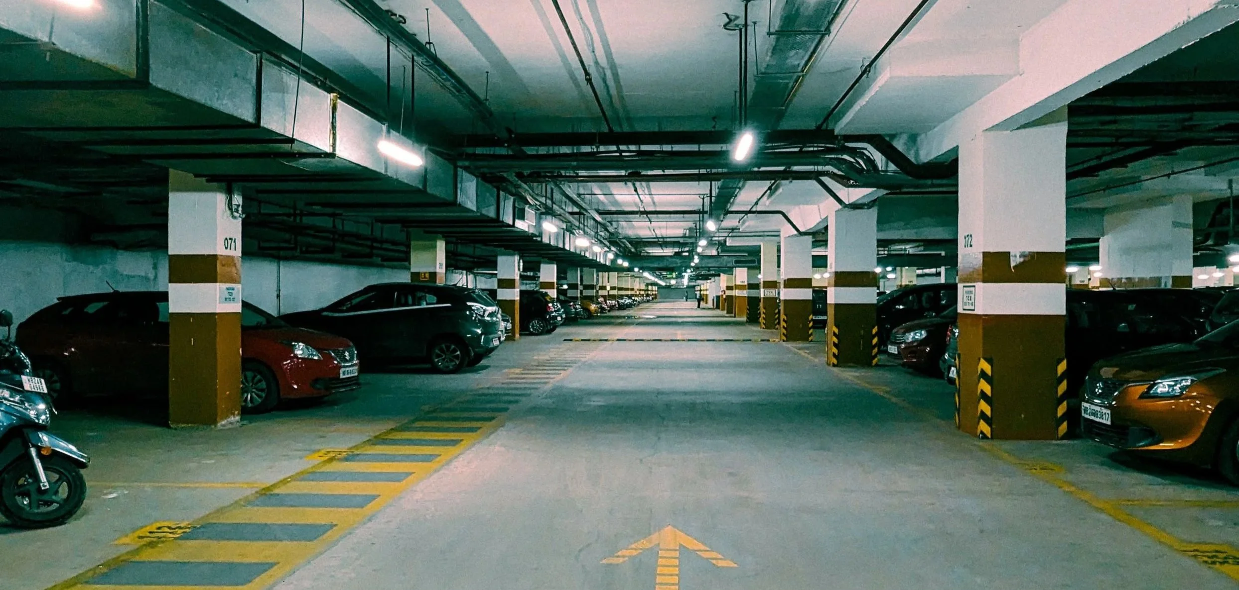Underground parking garage with multiple parked cars and a yellow directional arrow painted on the floor.