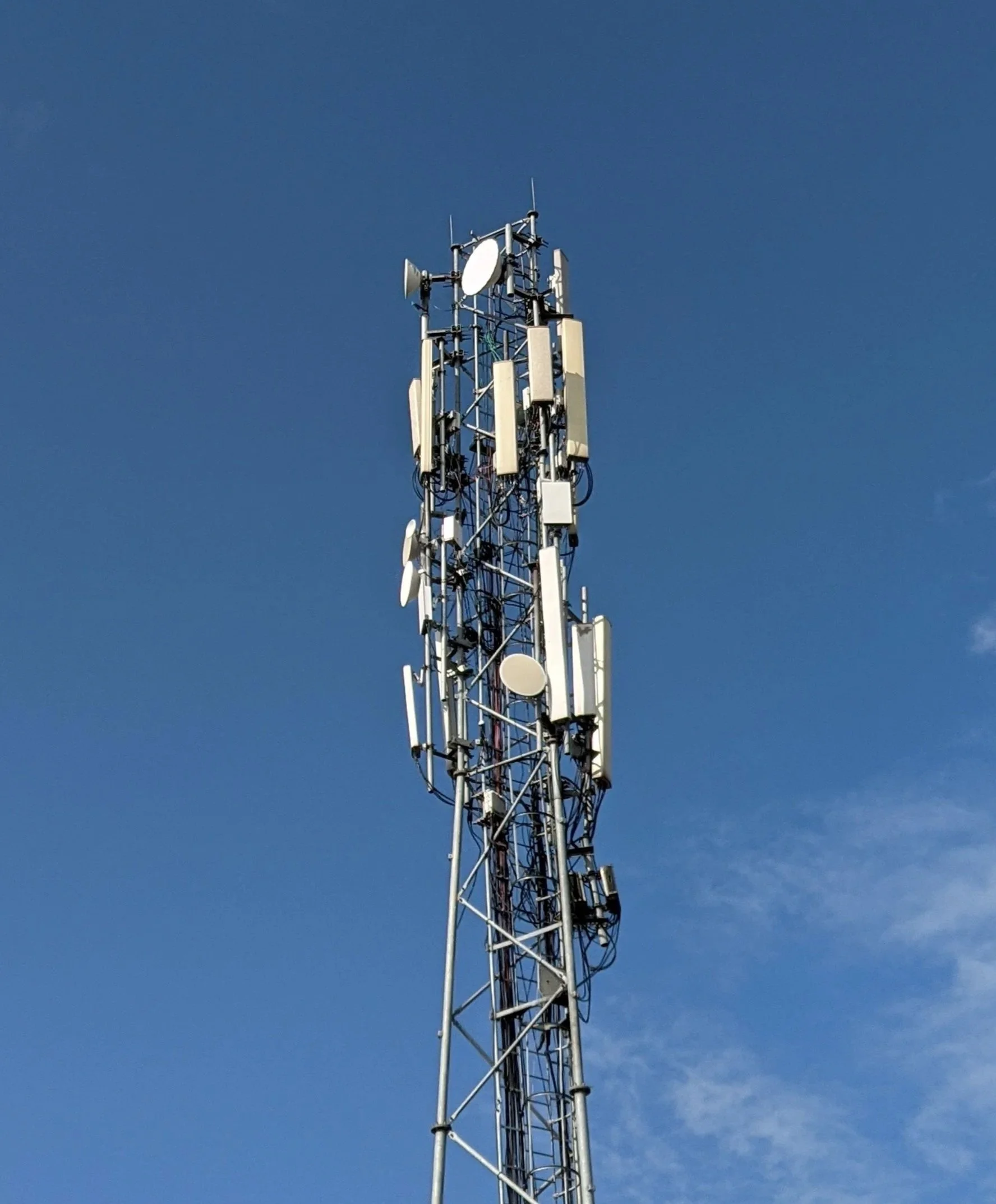 Communication tower with multiple antennas and satellite dishes against a clear blue sky.