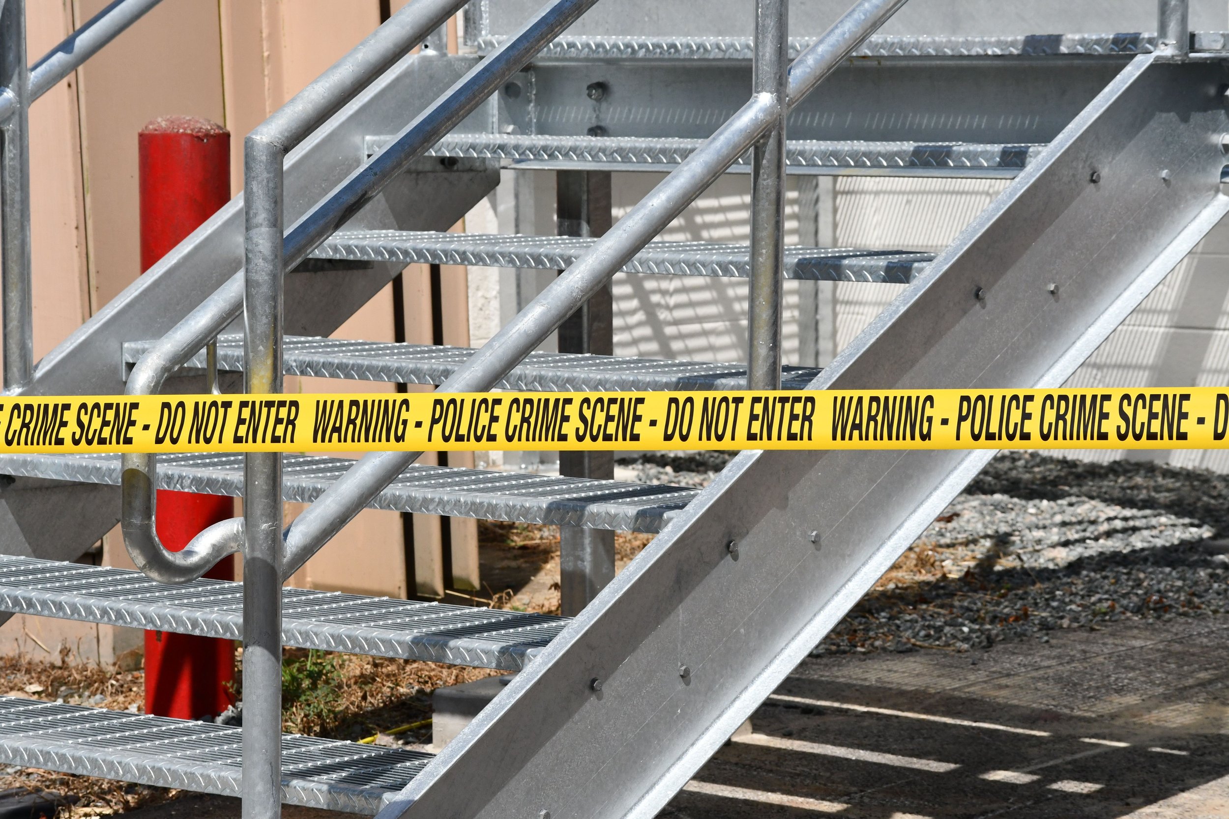 Metal outdoor staircase with yellow police caution tape that reads 'POLICE CRIME SCENE - DO NOT ENTER' wrapped around the railing.