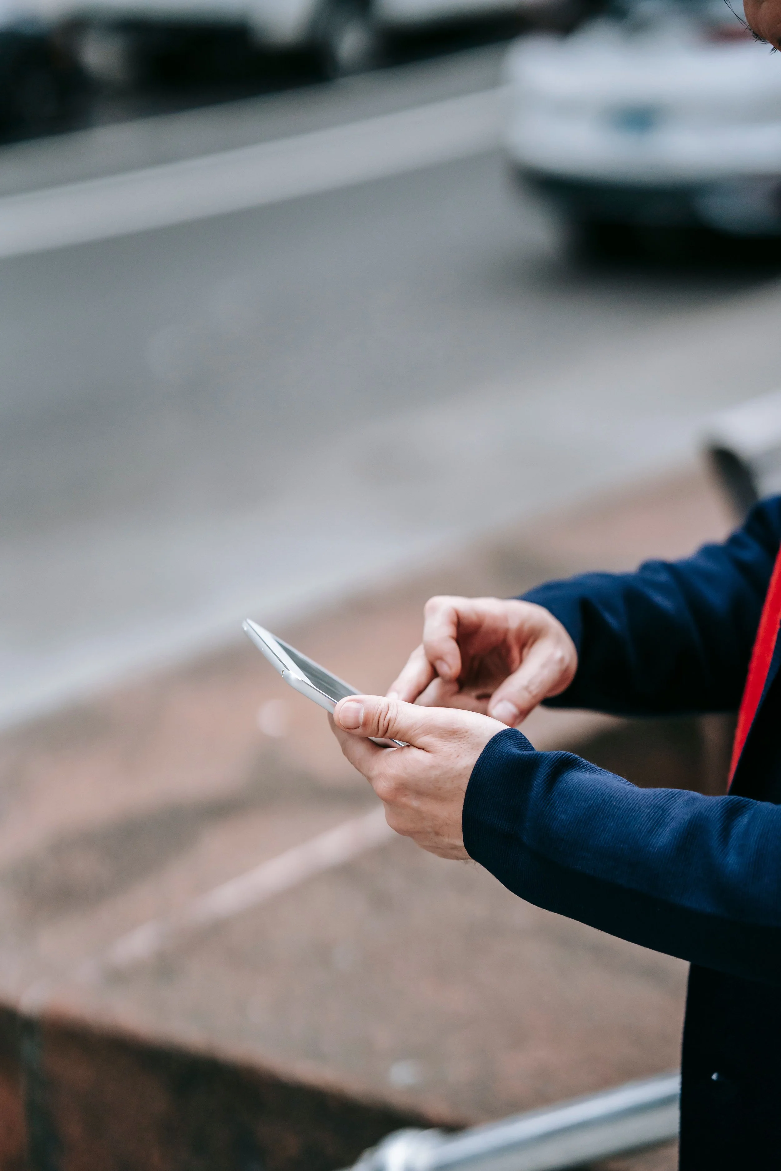 A person in a blue jacket holding and looking at a smartphone in their hands.