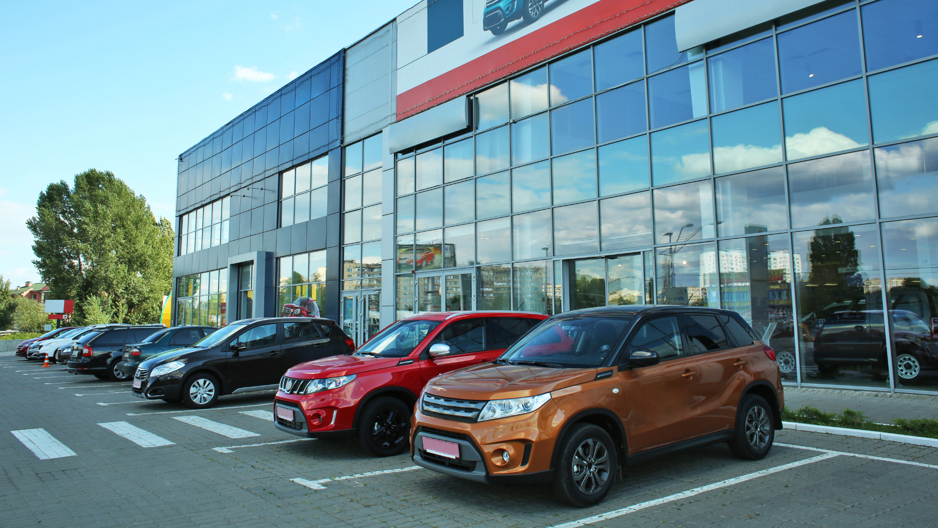 A car dealership with multiple cars parked in front of a glass building.
