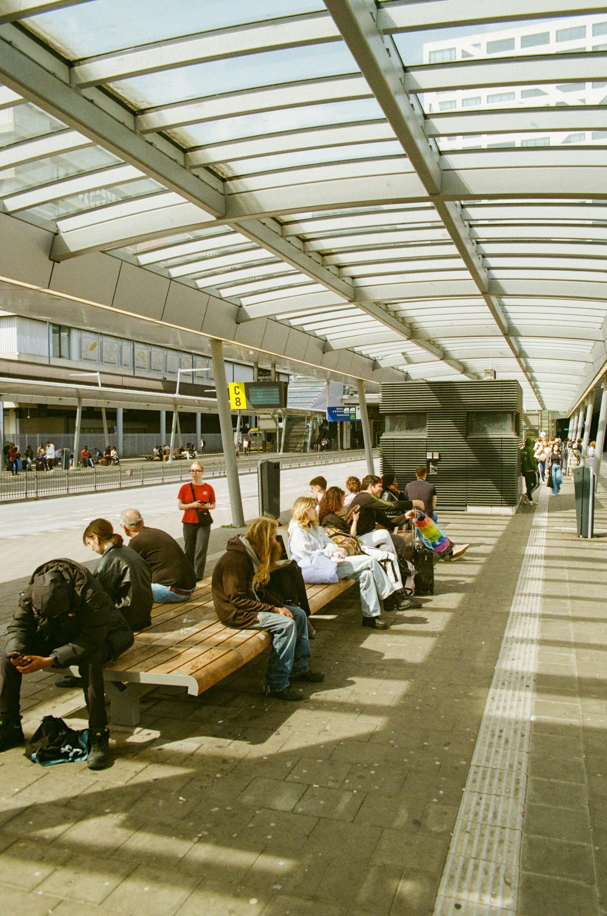 People sitting on benches at an outdoor train station platform under a glass canopy.