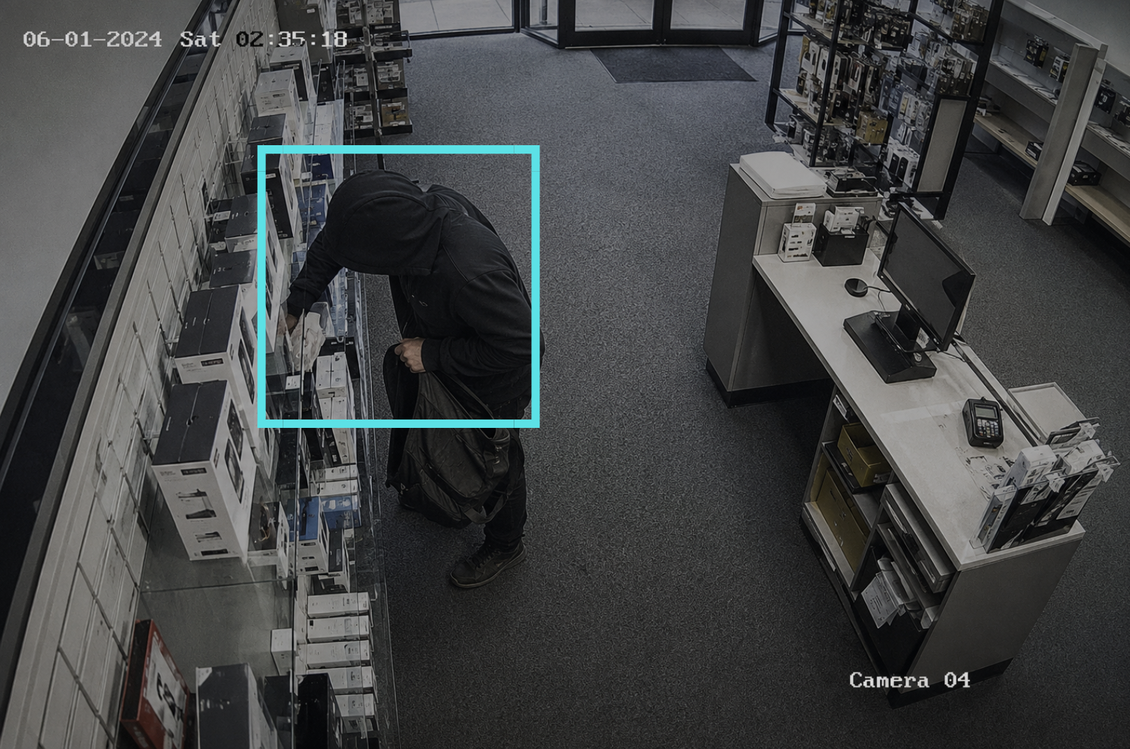 A person in a black hoodie and backpack placing store inventory into their backpack, with a blue rectangle overlay indicating active surveillance detection.