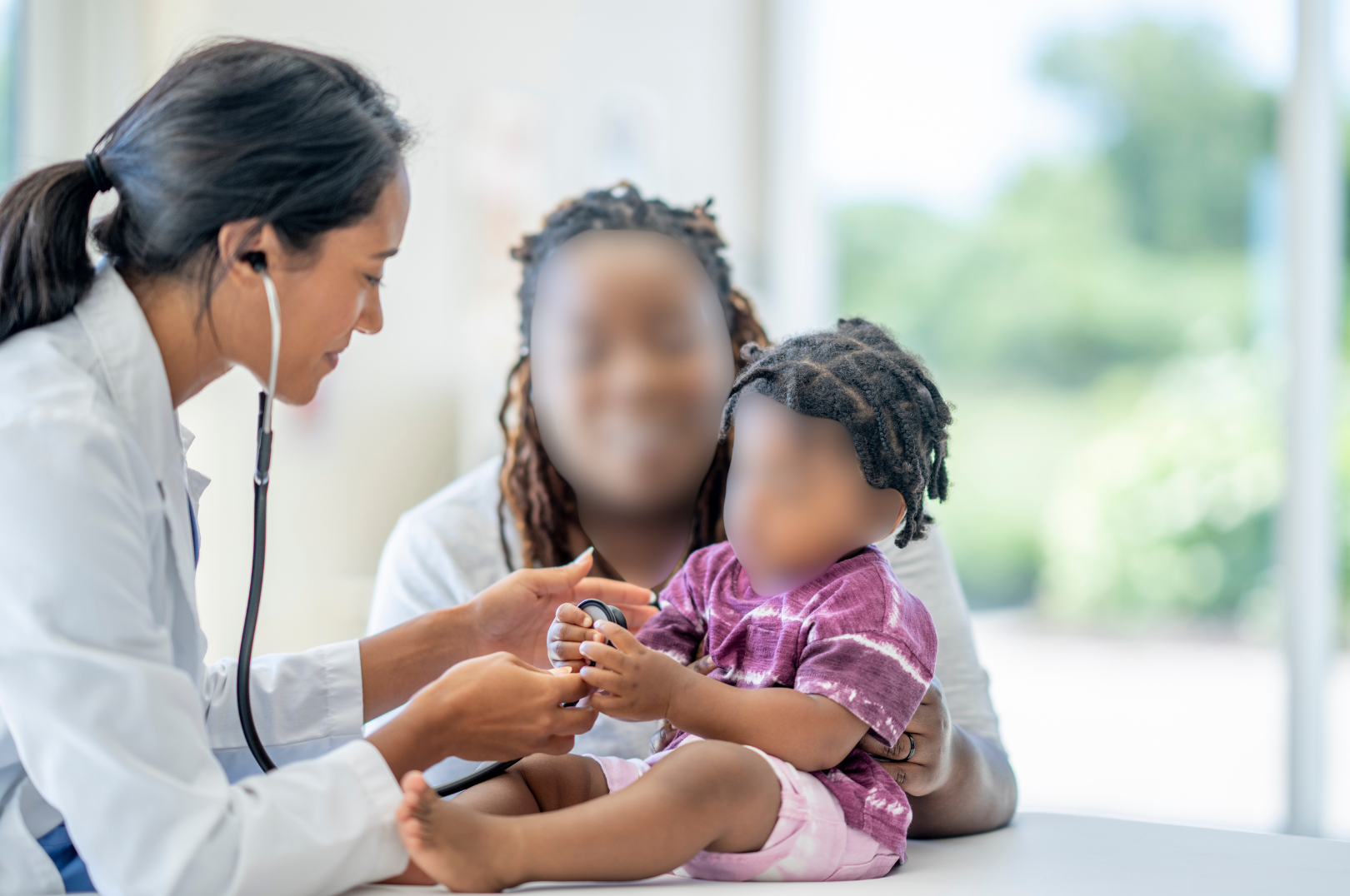 Doctor using a stethoscope on a young girl as her mom holds her. Both the mom and daughter's faces are blurred using ai privacy tools in a healthcare setting.