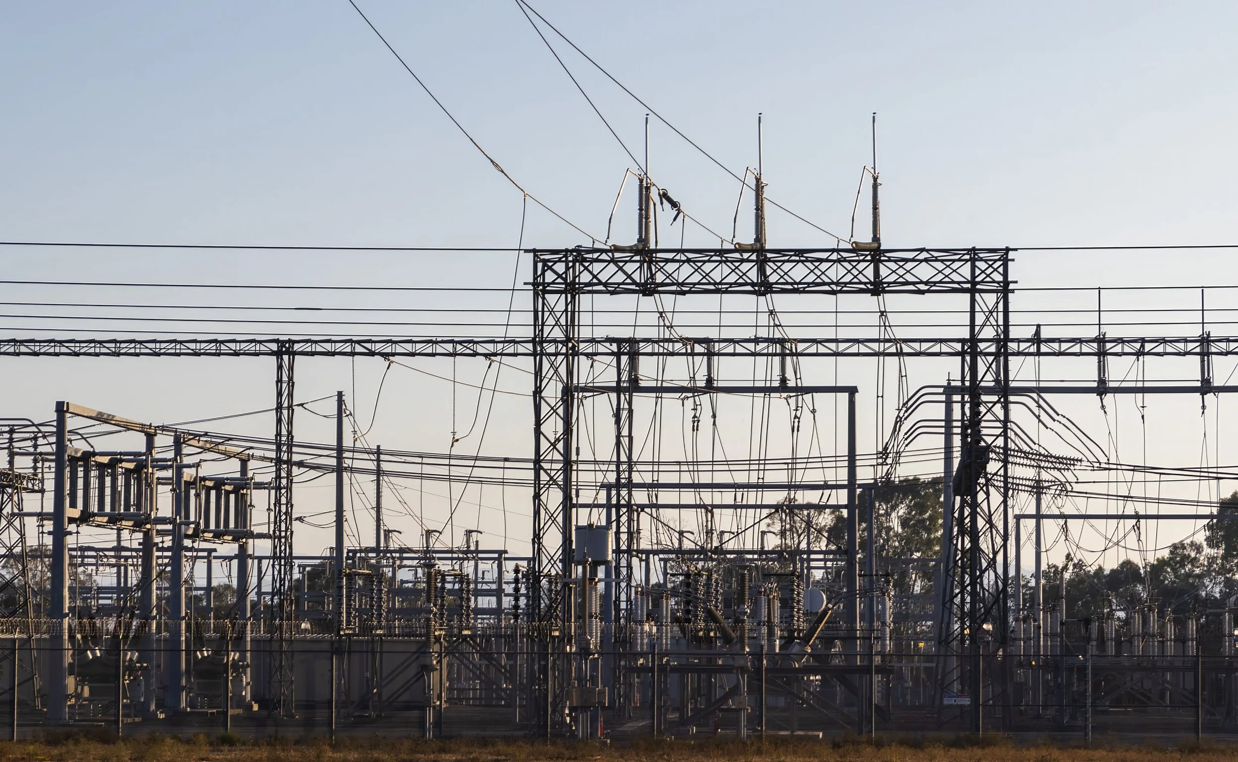 An electrical substation with multiple power lines, transformers, and steel structures under a clear sky.