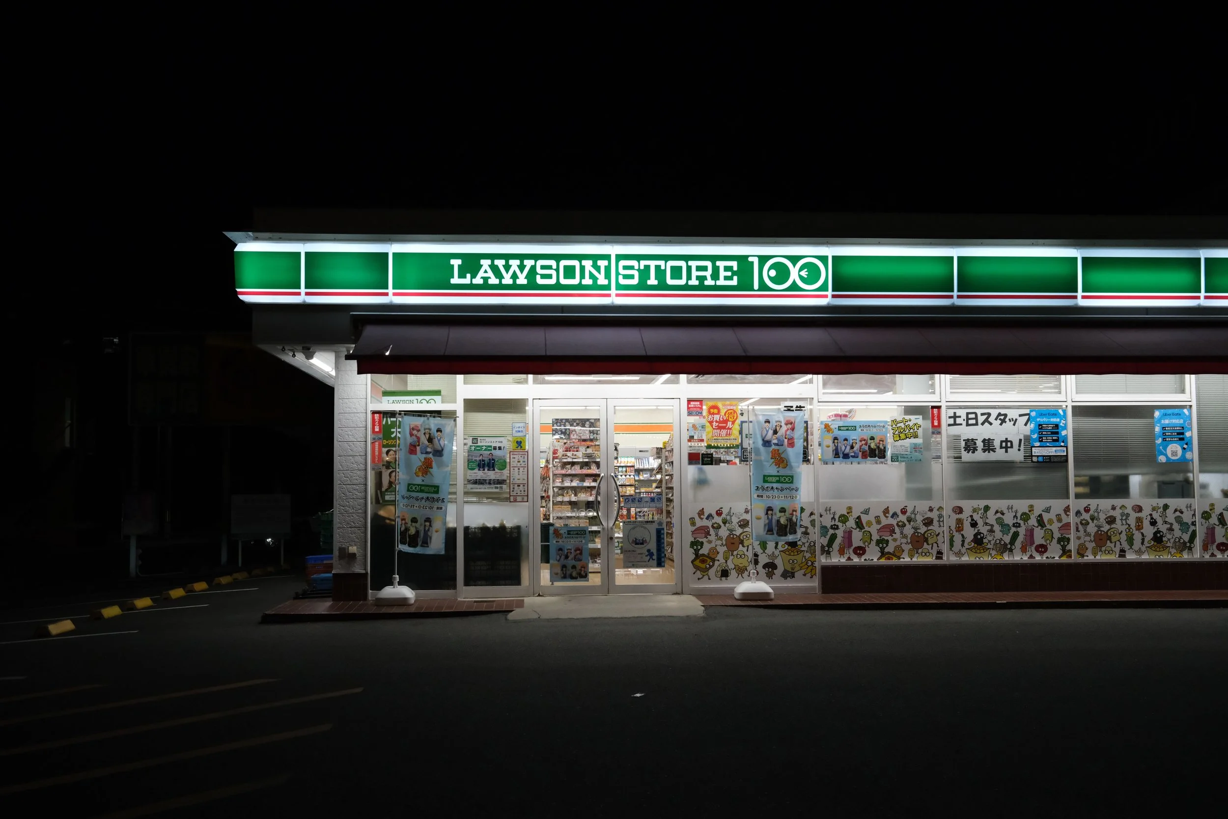 Nighttime exterior view of Lawson Store 100 convenience store illuminated with bright sign