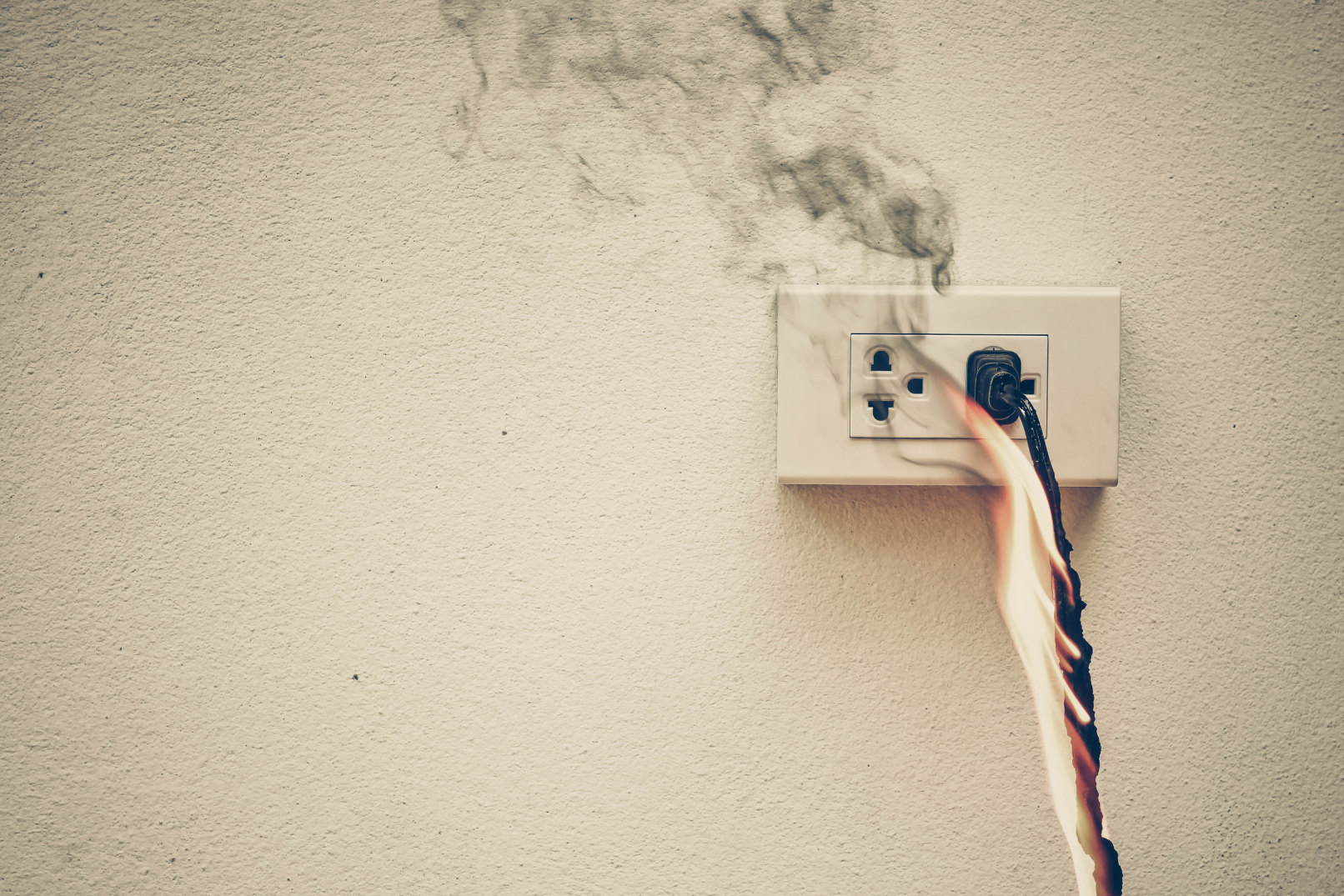 An electrical outlet on a beige wall with a burnt power cord and smoke coming from it.