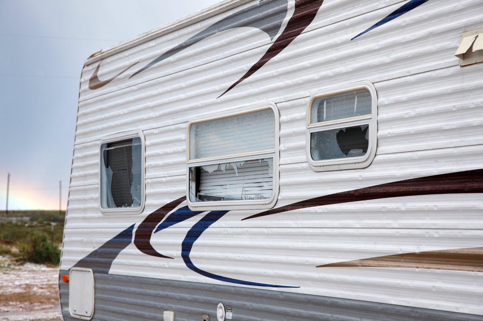 A trailer with broken windows and some damage, set against a cloudy sky and a distant horizon.