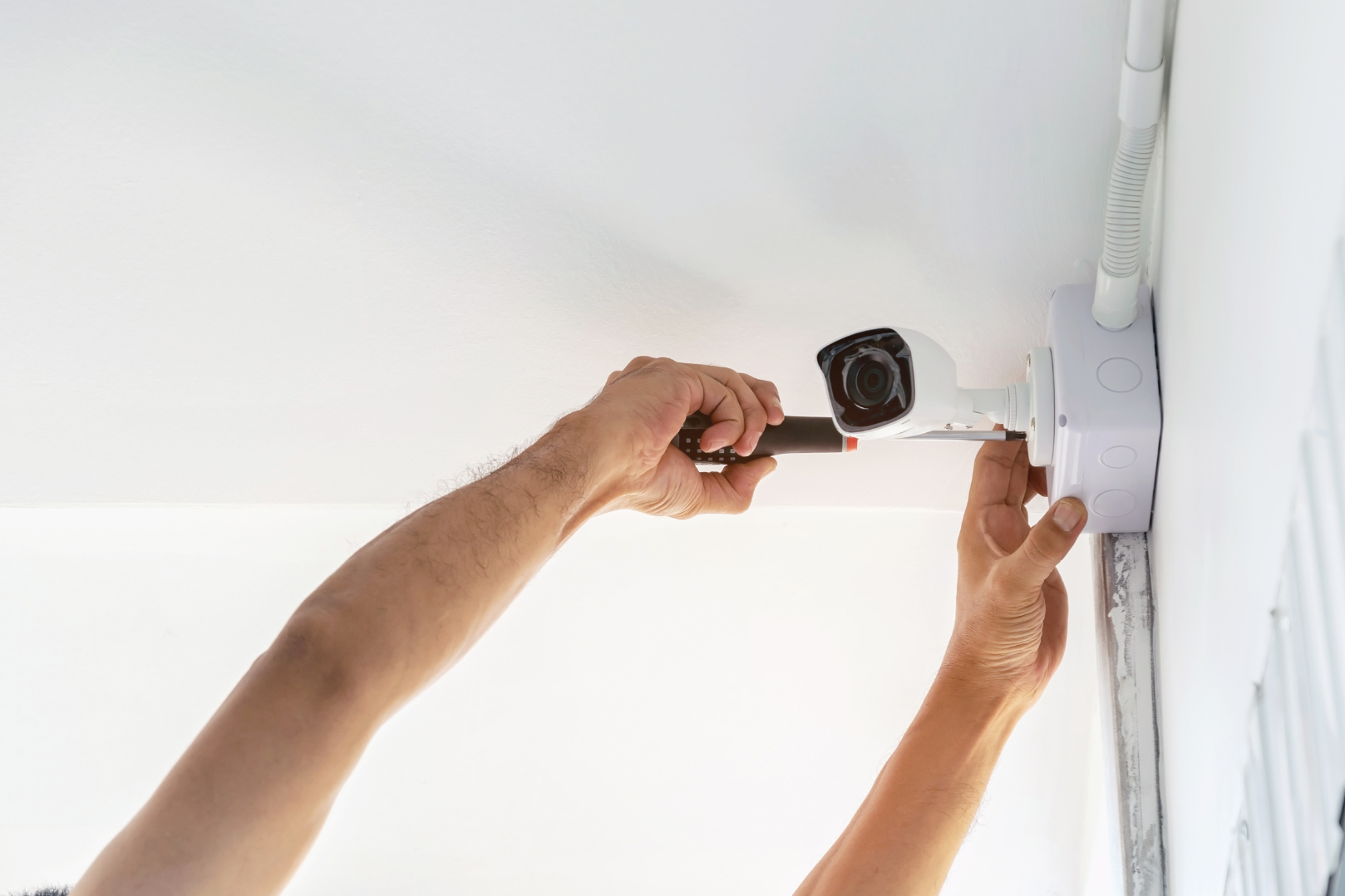 A person installs a security camera on a ceiling using a screwdriver.