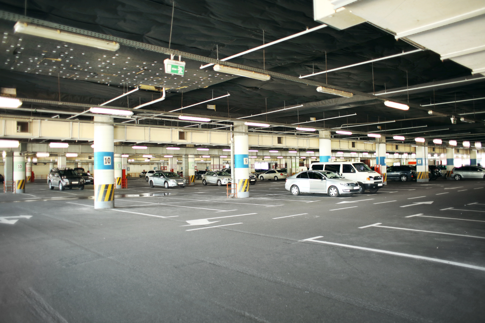 Indoor parking garage full of parked cars with numbered columns and green exit sign.