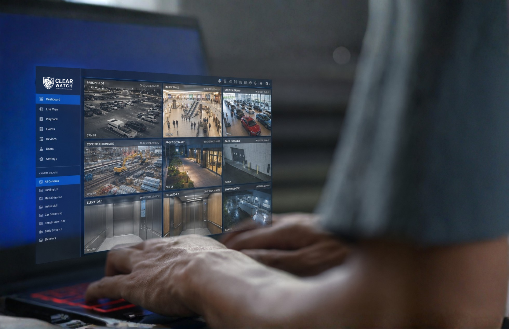 A person monitoring security camera footage on a computer screen, showing multiple views of a parking lot, mall interior, construction site, and different entrances and elevators.