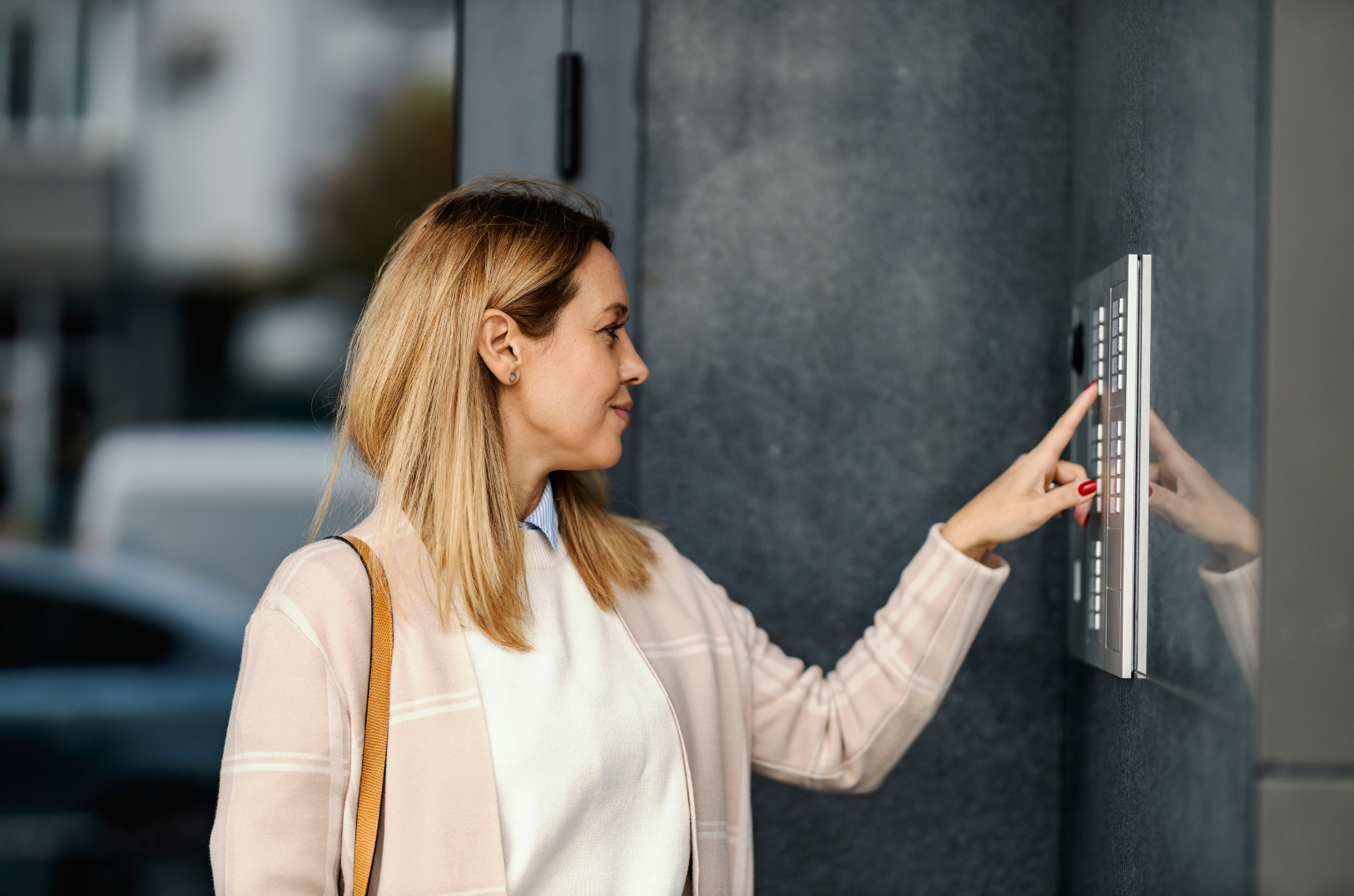Woman pressing a button on an intercom system on a dark stone wall outside a building