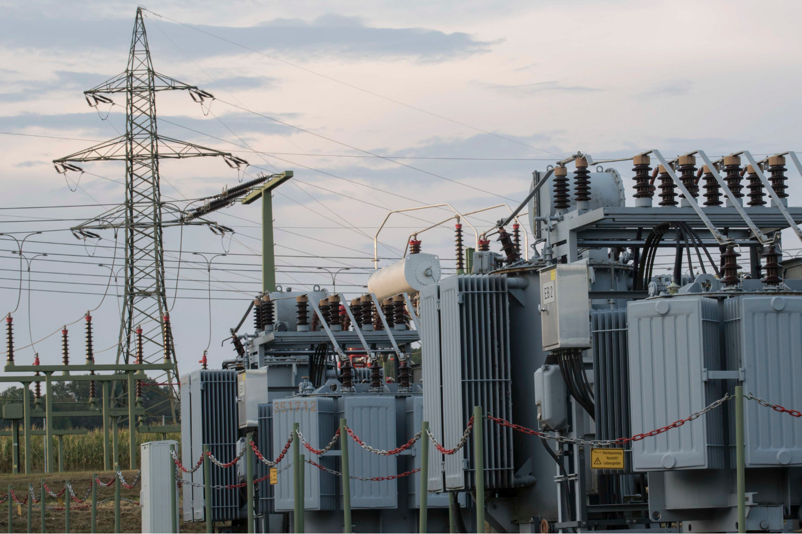 Electrical transformers and high-voltage power lines against a partly cloudy sky.