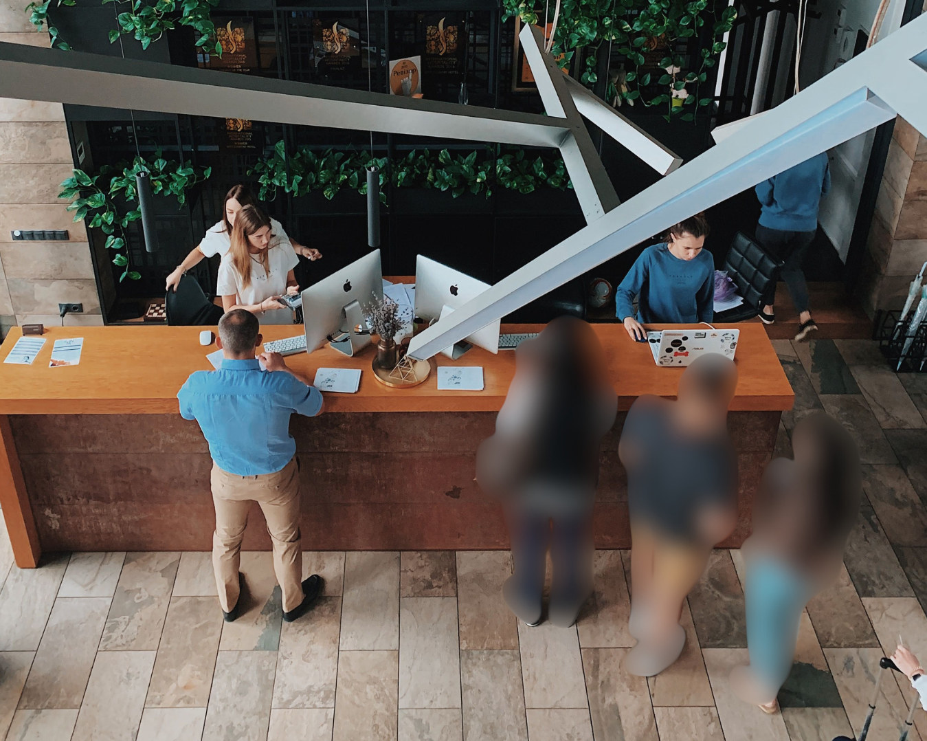 View of a busy hotel reception desk with staff and guests, seen from above, with people checking in and chatting. All customers are blurred using privacy ai tools.