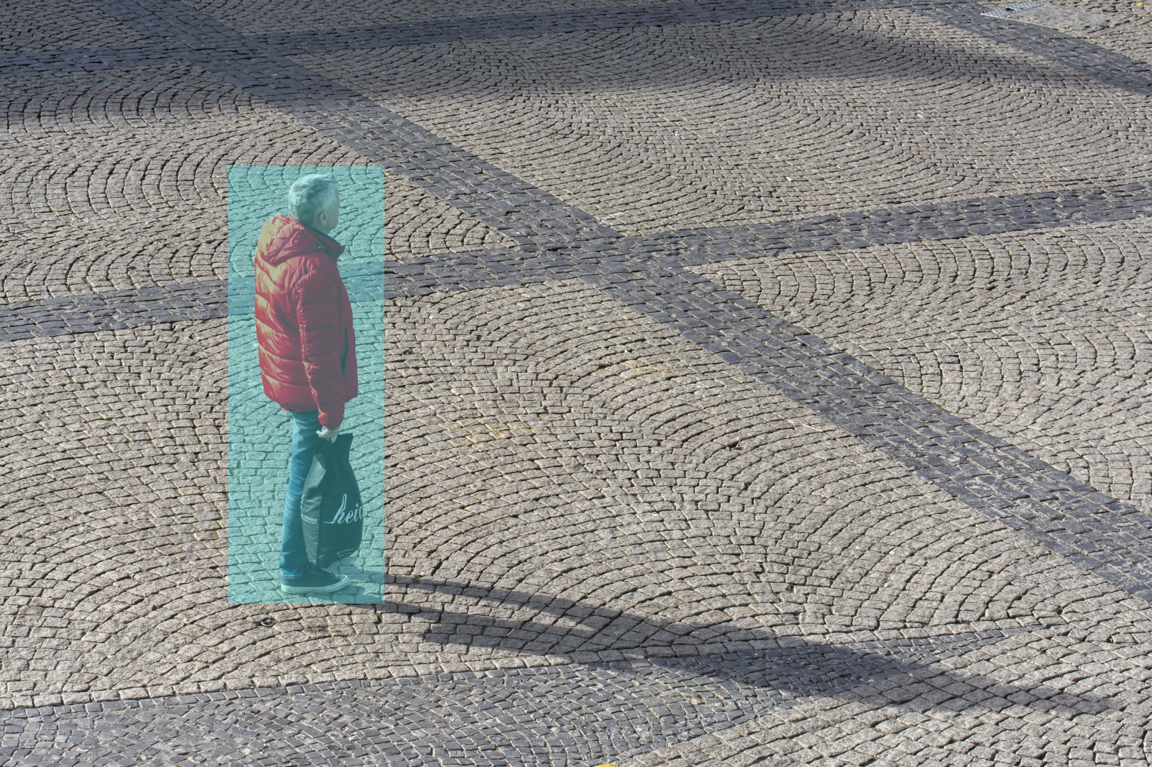 A man wearing a red jacket and jeans standing on a cobblestone street, holding a shopping bag, highlighted in blue by ai surveillance.