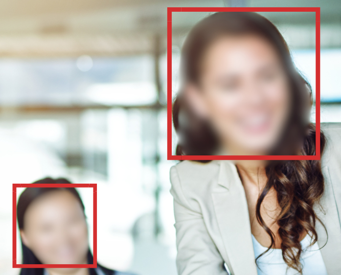 Two women in an office setting, with the woman in the foreground smiling and the woman in the background also smiling, both wearing business attire, both woman highlighted by red rectangles signifying identification.