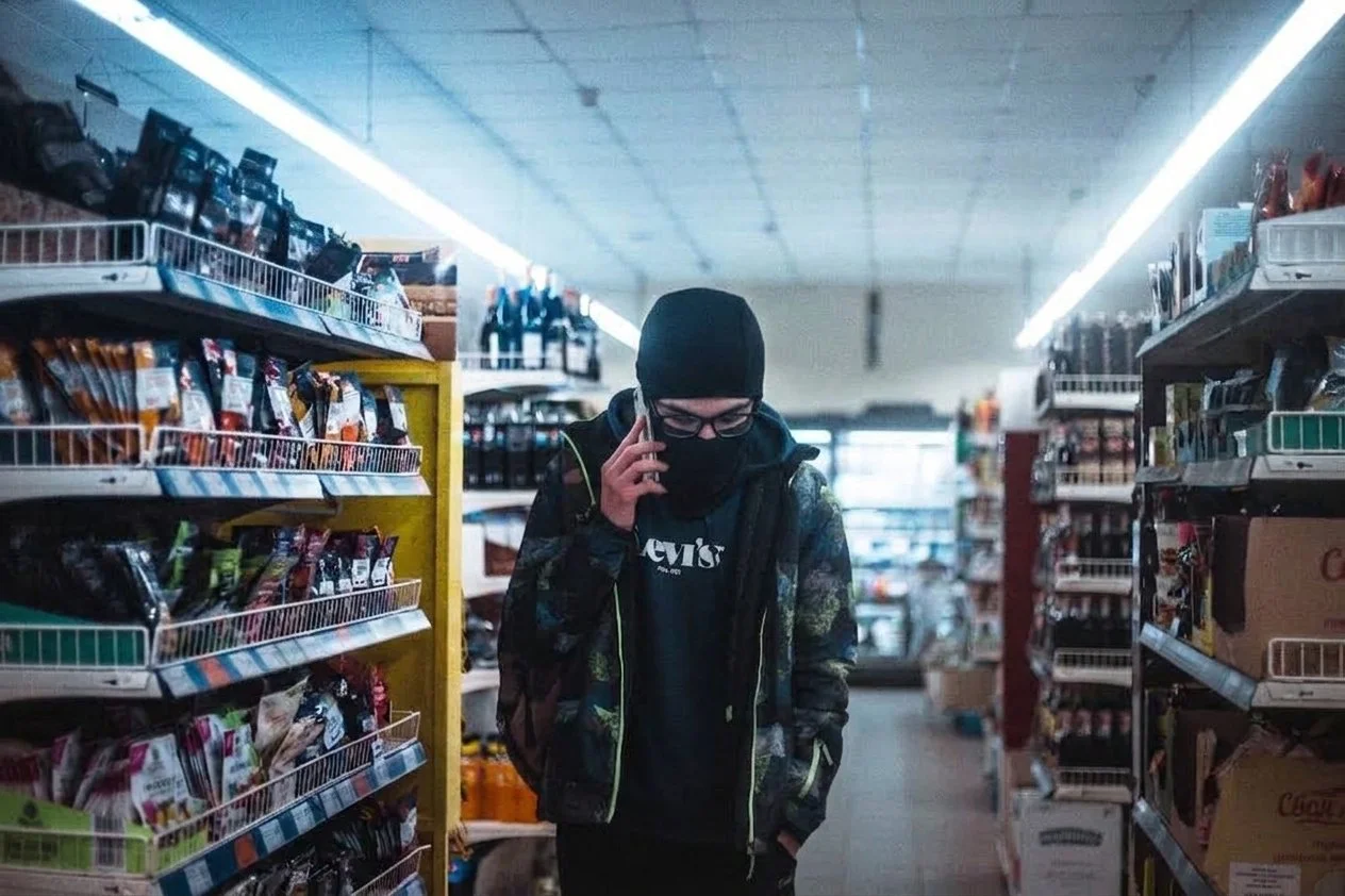 A suspicious person wearing a ski mask is walking around a convenience store.