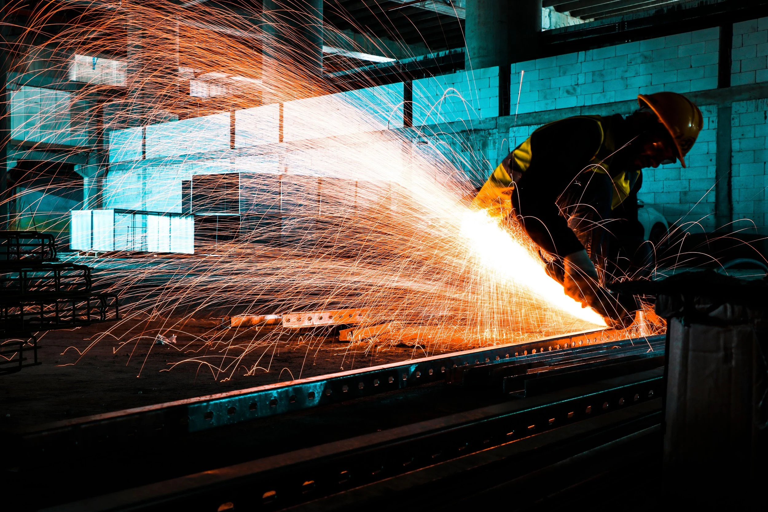 A worker welding metal inside an industrial warehouse with sparks flying.