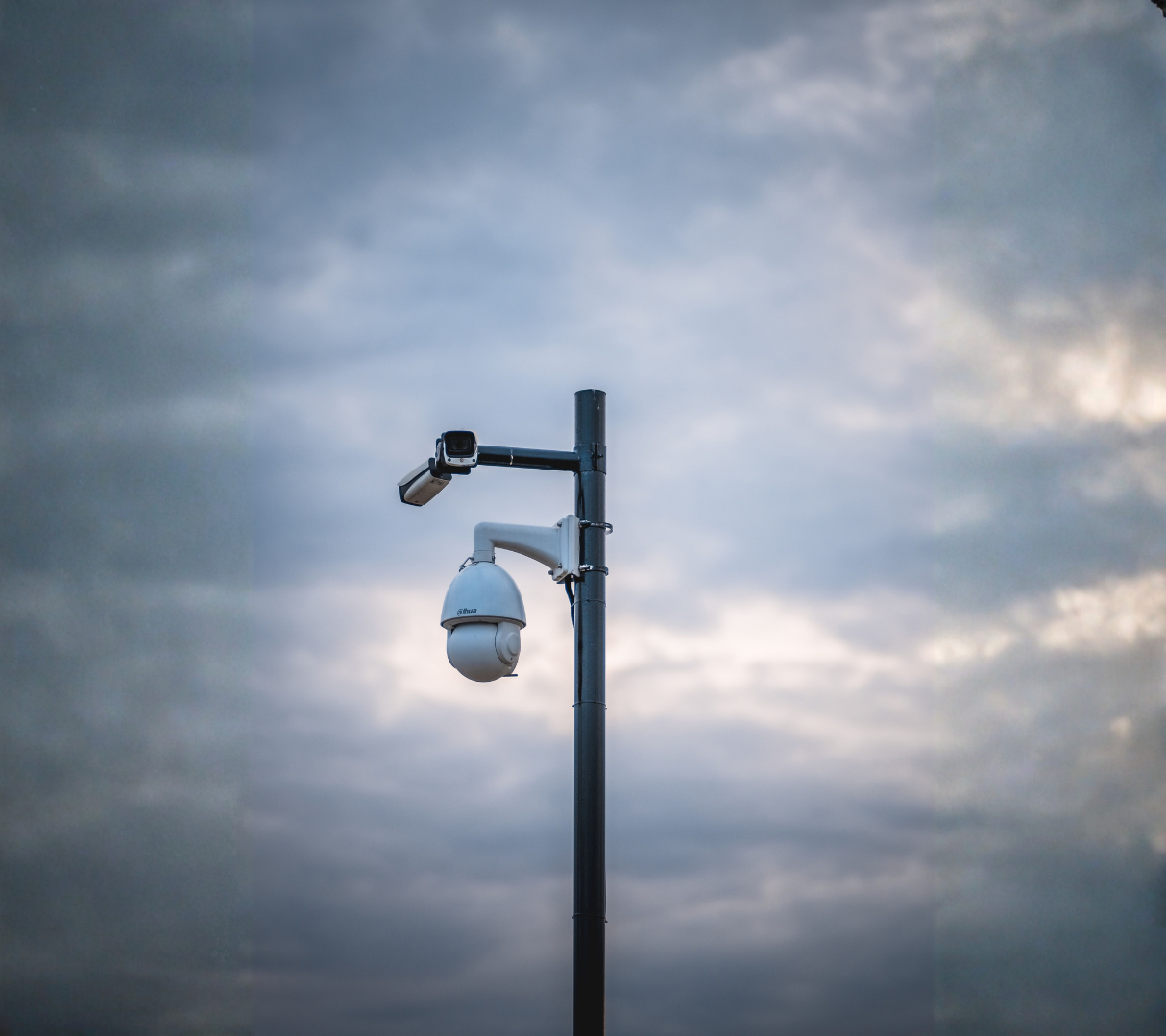 Security camera mounted on a tall pole against cloudy sky.
