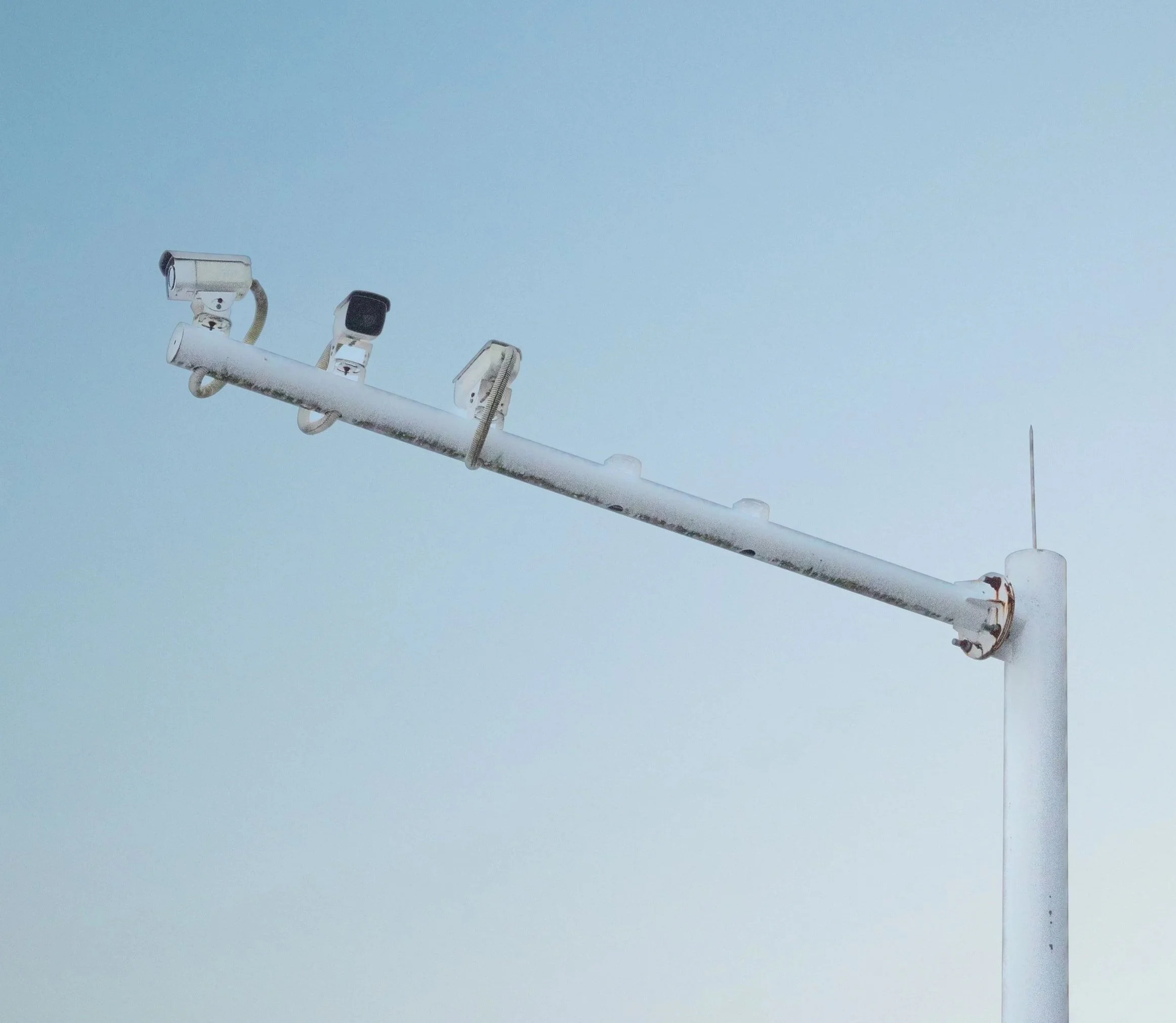 Close-up view of a white street light with three fixtures against a clear blue sky.