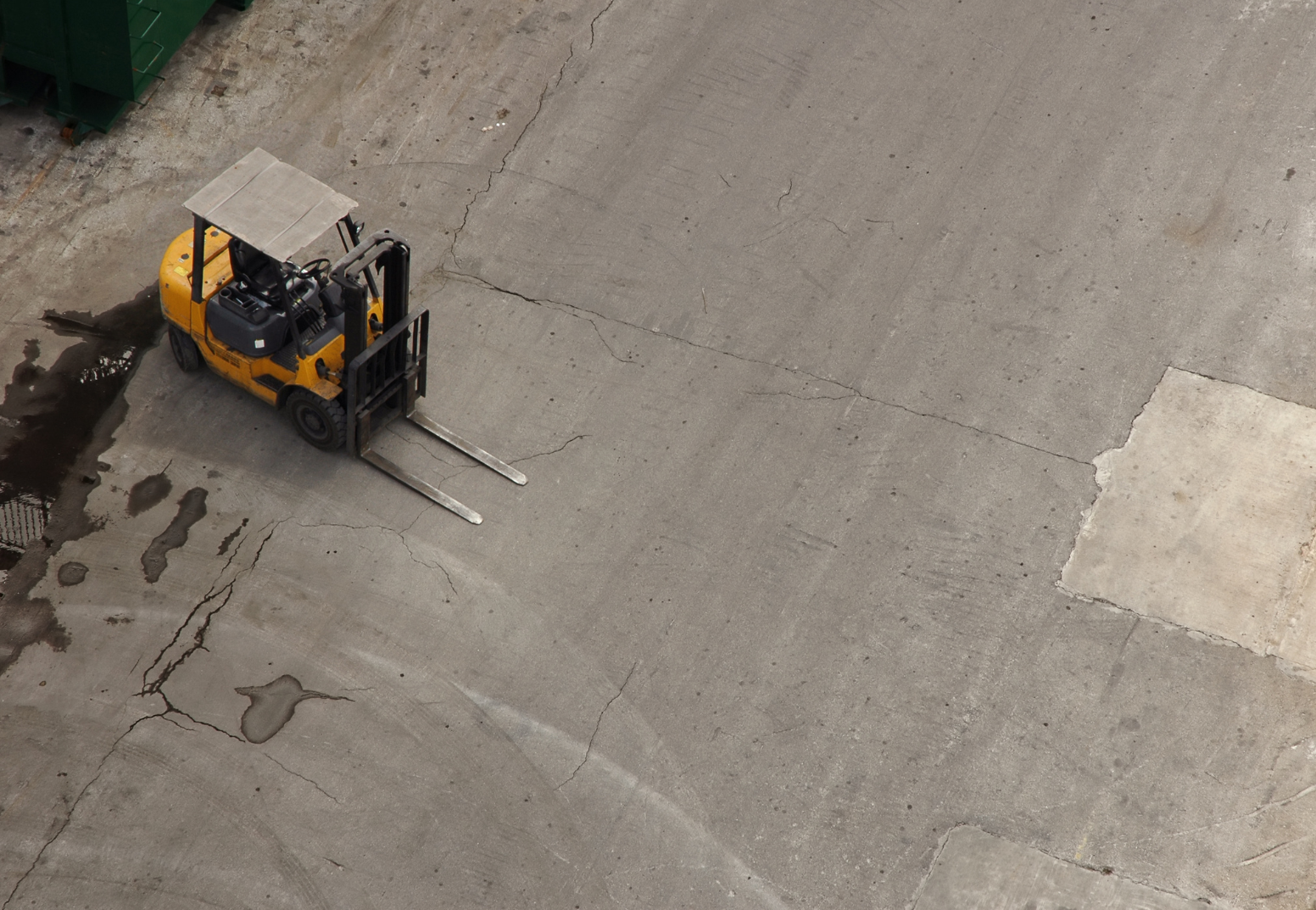A yellow forklift truck parked on a cracked concrete surface with puddles of water nearby.