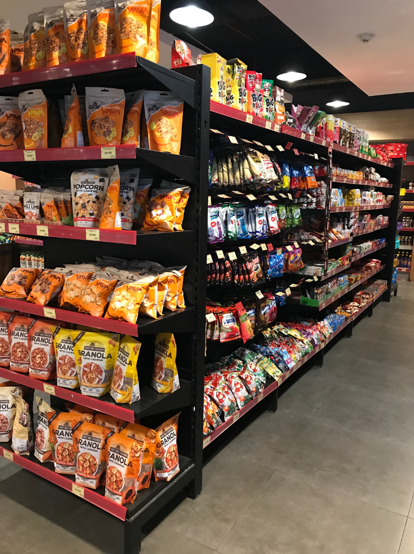 A grocery store aisle featuring shelves stocked with various snack foods such as popcorn, granola, and chips in colorful packaging.