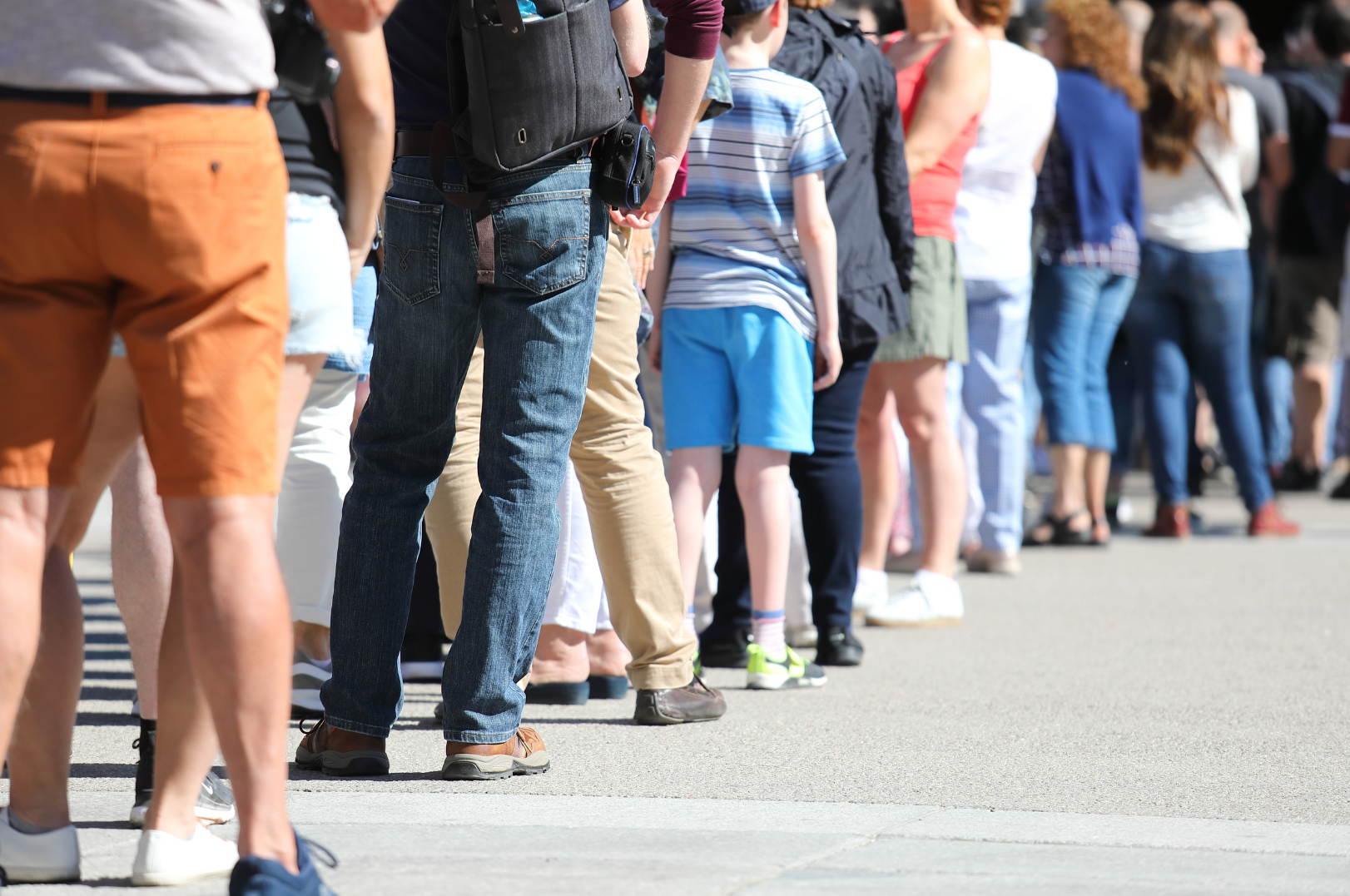 A line of people standing outdoors on a sunny day.