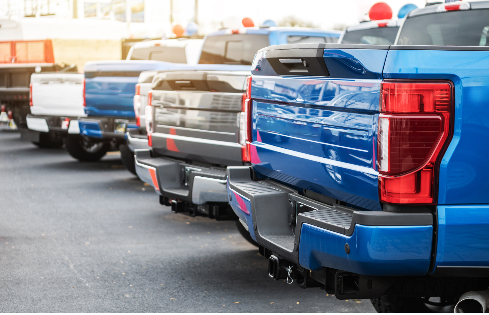 Multiple pickup trucks in different colors parked in a row on a paved lot, with red and blue emergency lights on their roofs.