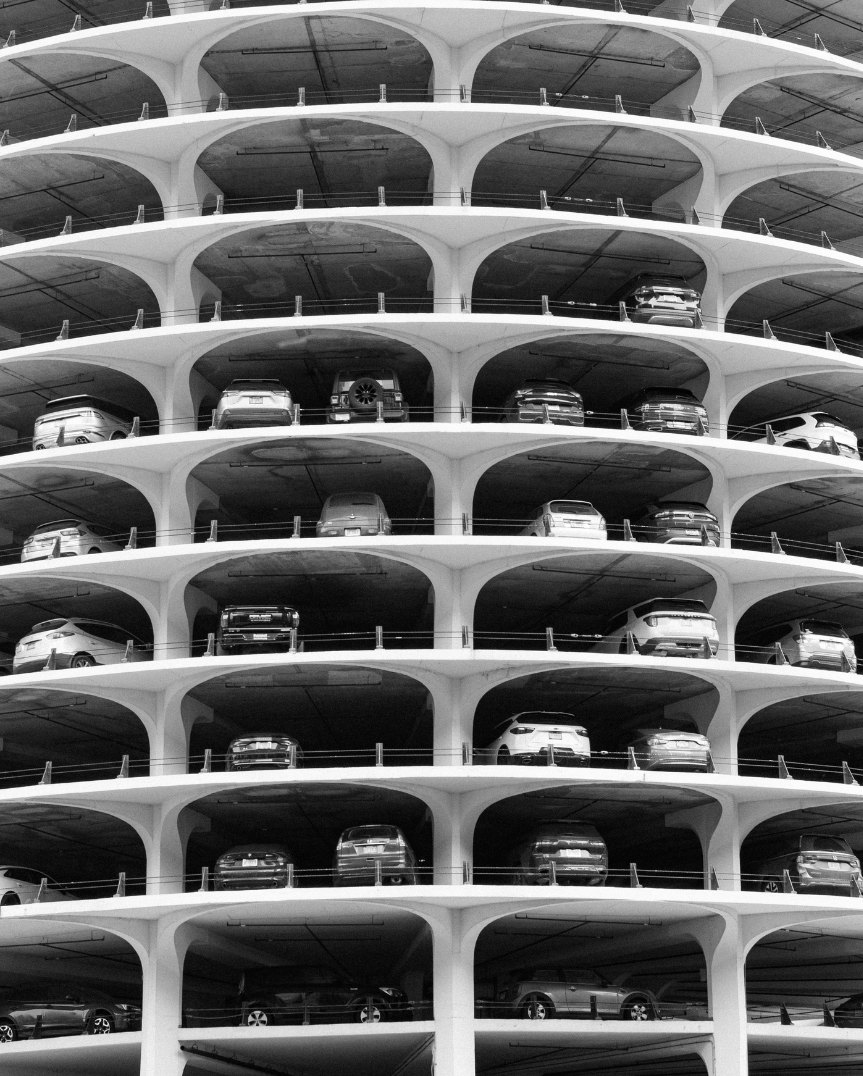 A black and white photograph of a multi-level parking garage with cars parked on each floor.