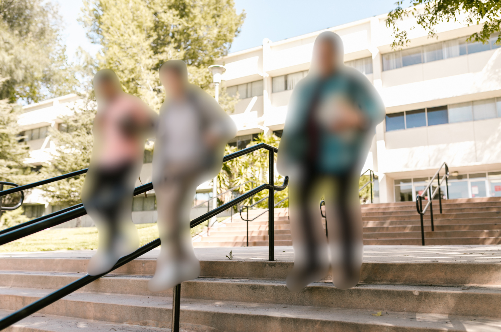 Three college students walking away from a campus building, walking down an outdoor staircase. All 3 students are blurred using privacy ai.
