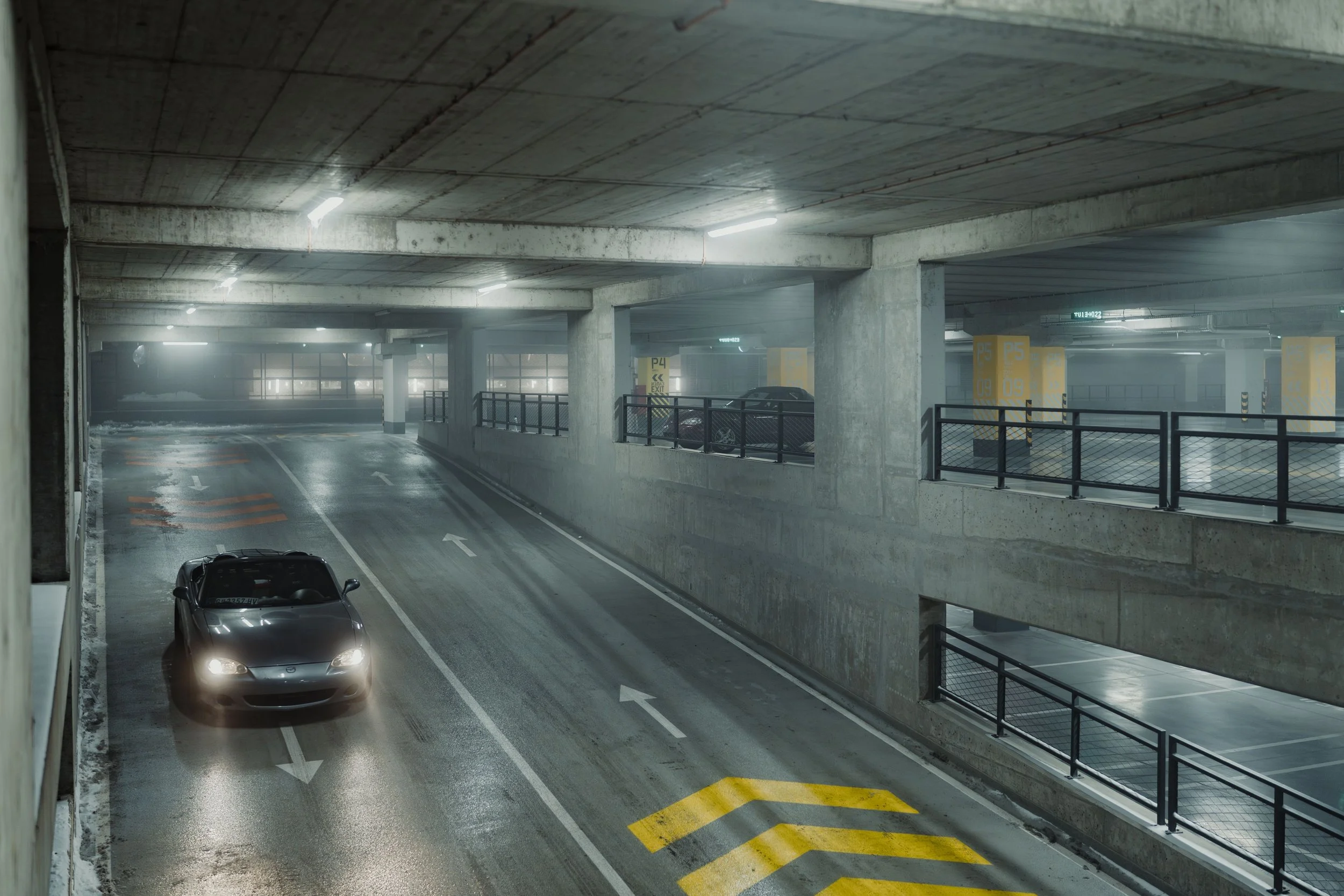 Underground parking garage with concrete pillars, parked cars, and yellow p4 parking sign with a car exiting the garage.