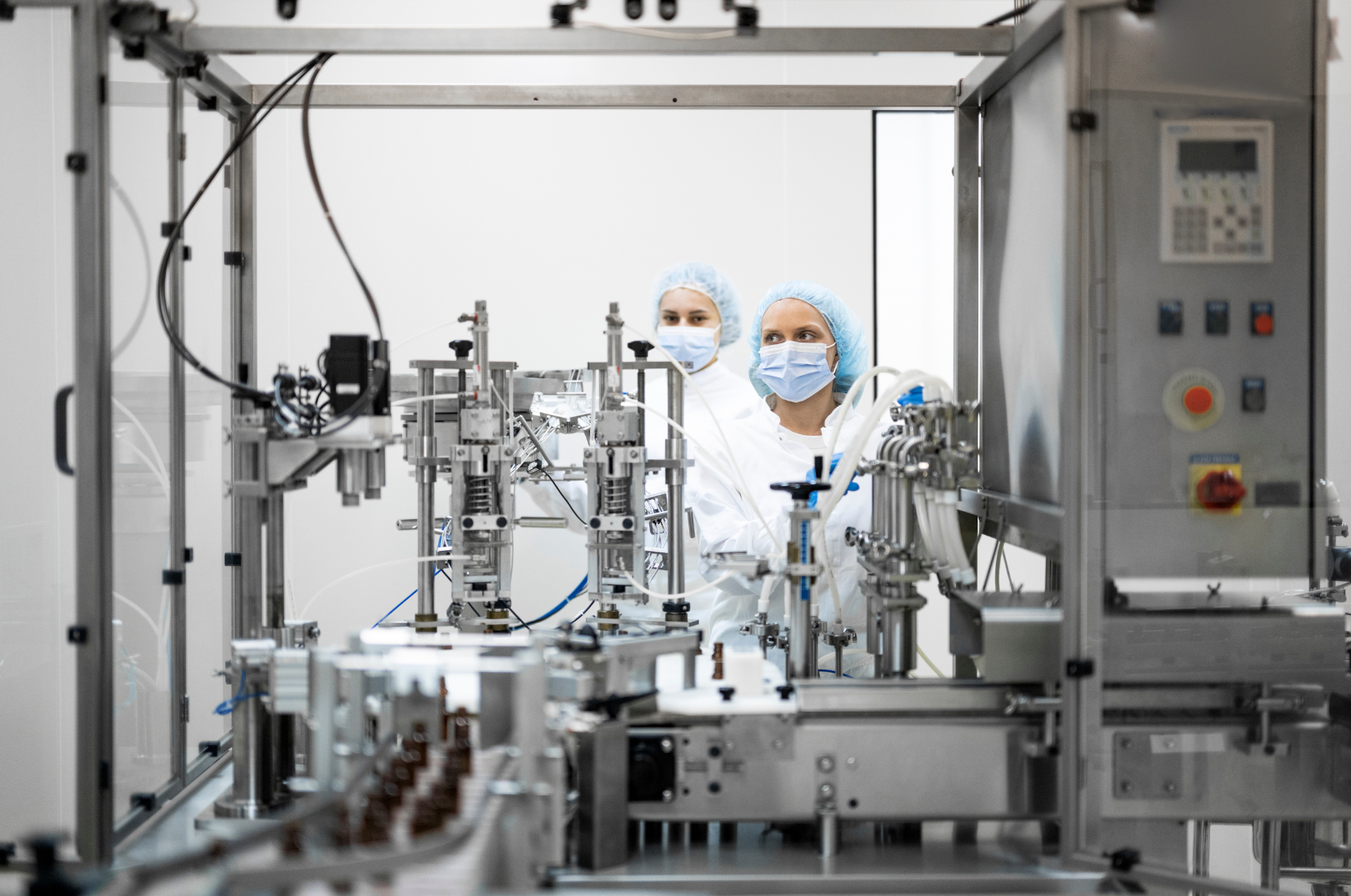 Two scientists wearing masks and hair covers working on a complex piece of machinery in a laboratory.