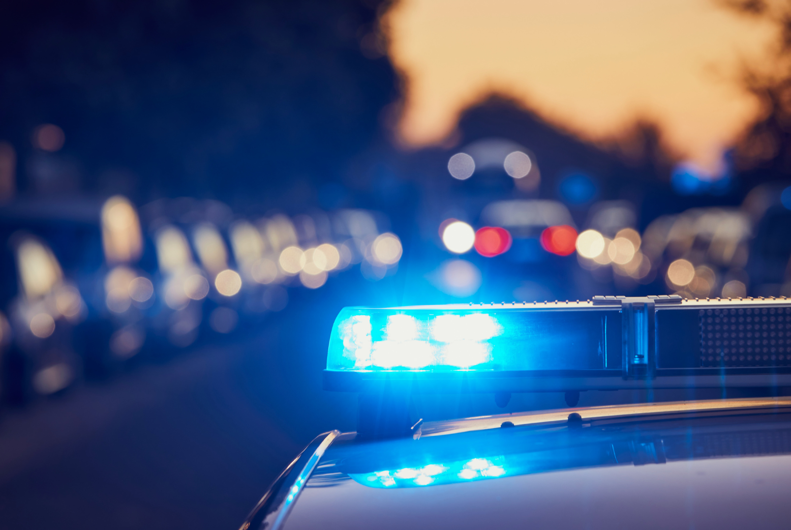 Police car with flashing blue lights at night, blurriness of other vehicles and streetlights in the background.